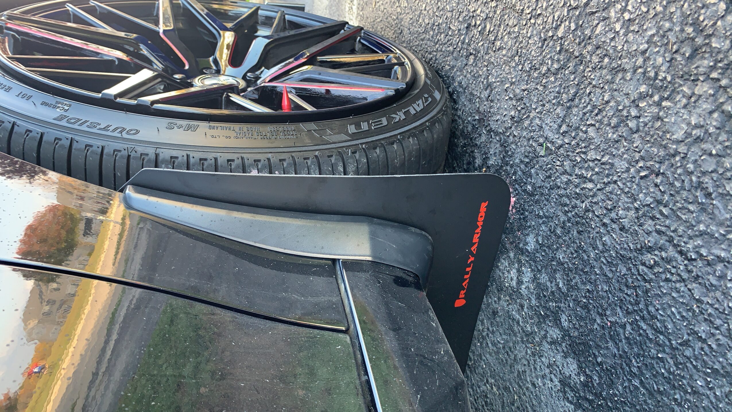 Close-up of a car's rear wheel and part of the rear wing on a paved surface.