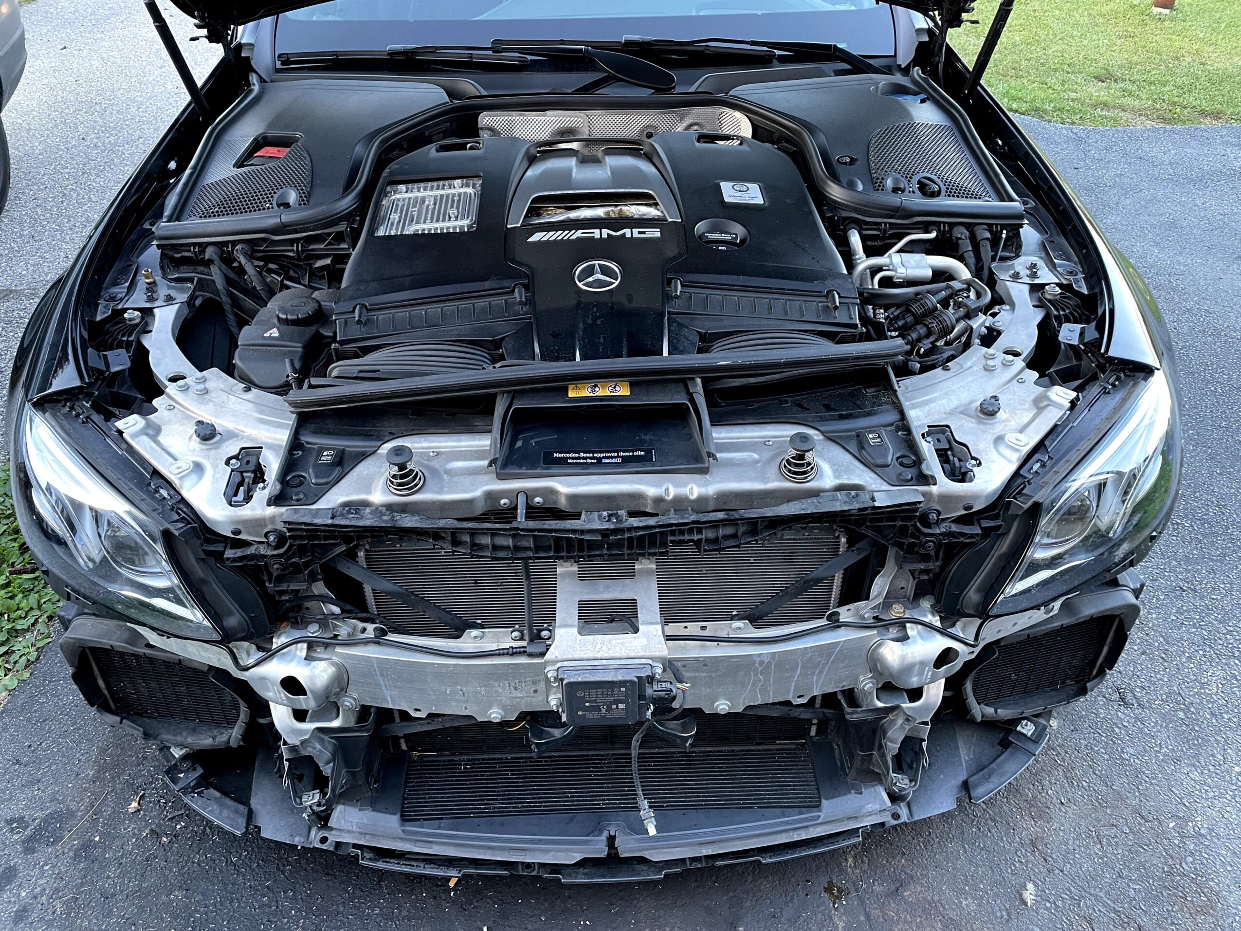 Front view of a car with the hood open, showing the engine and internal components, parked on a driveway.
