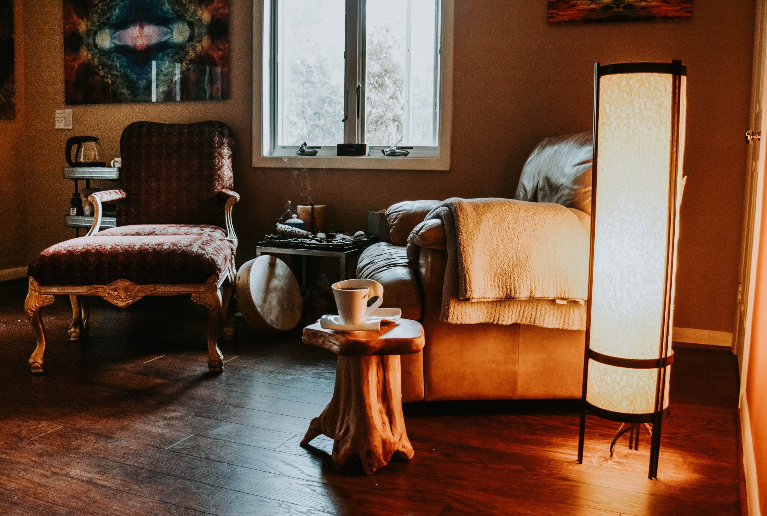 Living room with armchair, sofa, window, and floor lamp, illuminated by warm lighting.