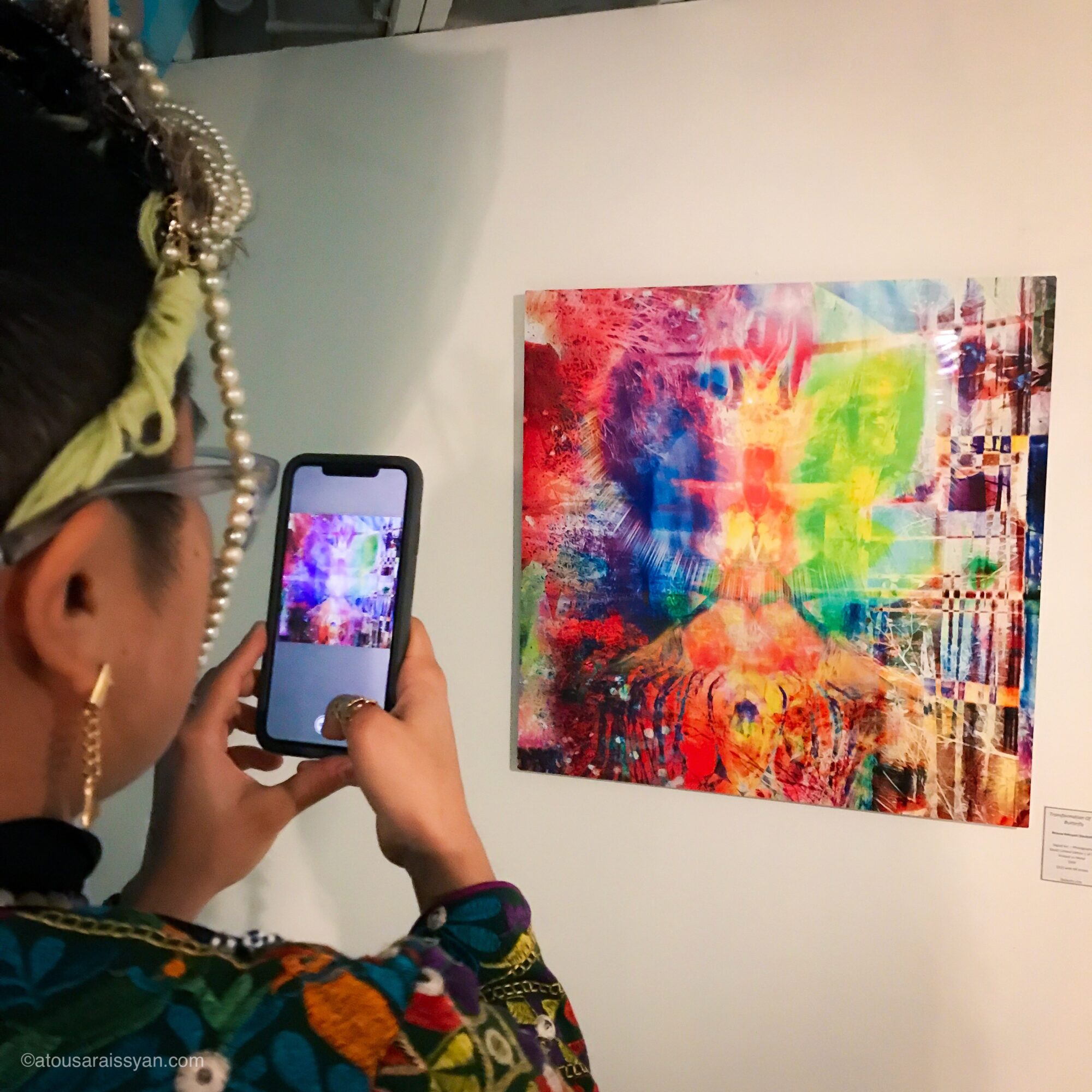 Person taking a photo of a colorful abstract painting with a smartphone in an art gallery.