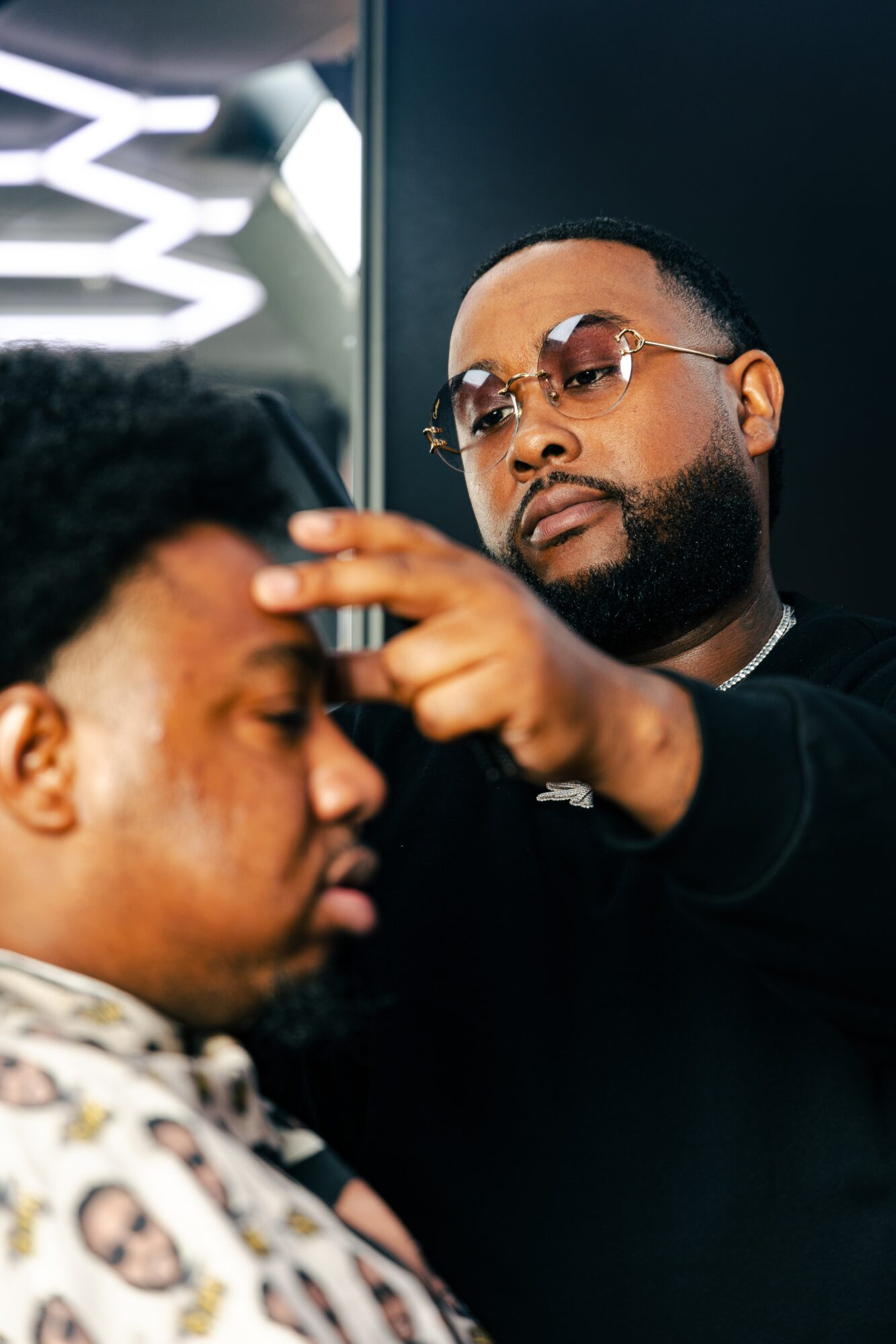 Barber trimming a young man's hair in a modern salon, with a mirror and bright lighting in the background.