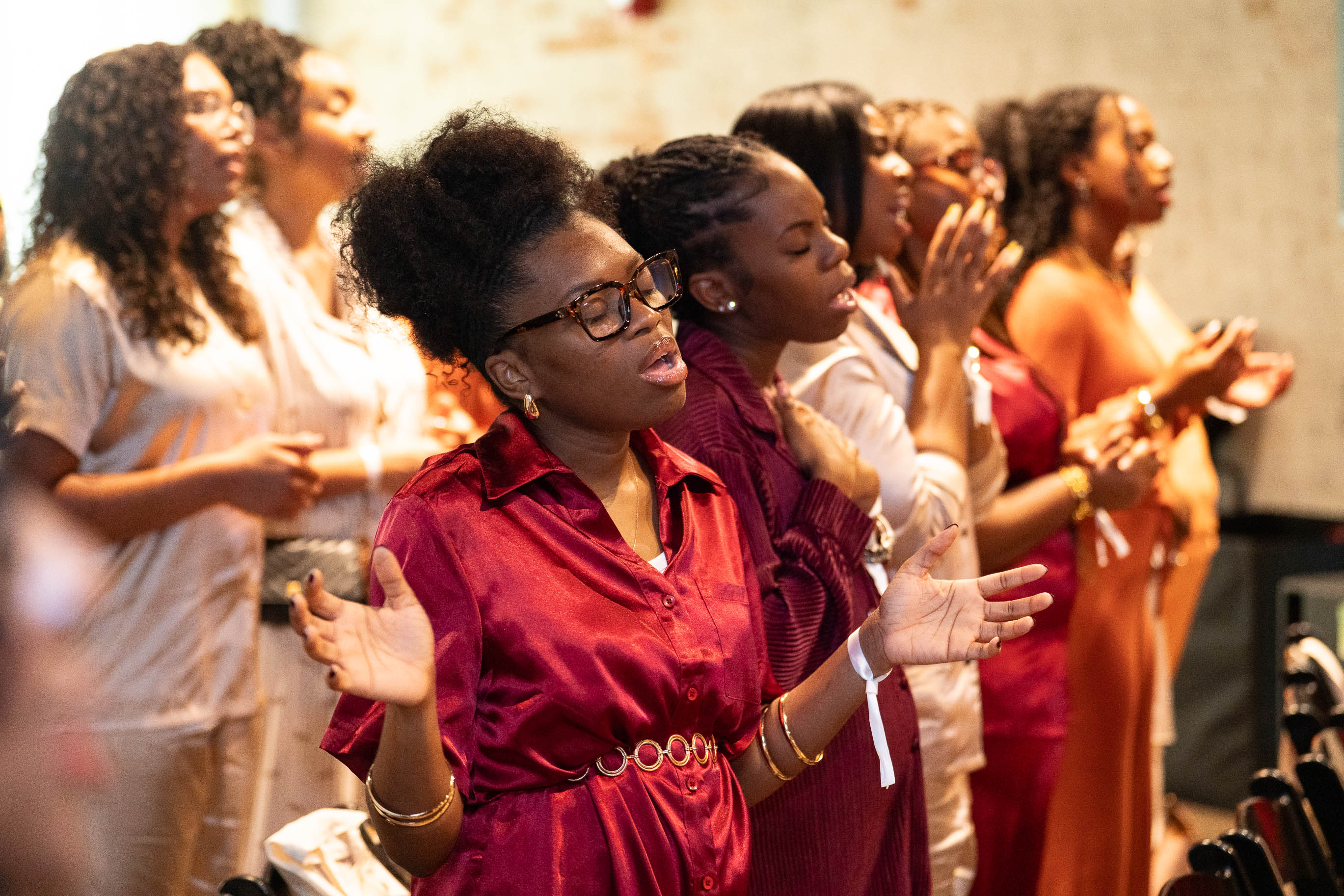 Group of women with eyes closed, hands raised, and clapping, participating in a spiritual or religious gathering.