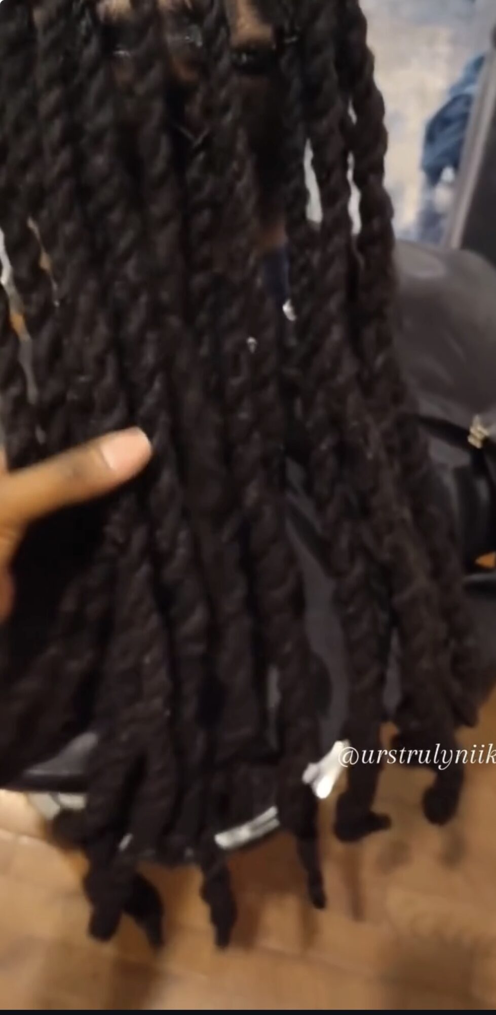 Close-up of long, thick, twisted braids with beads at the ends, held by a person's hand.