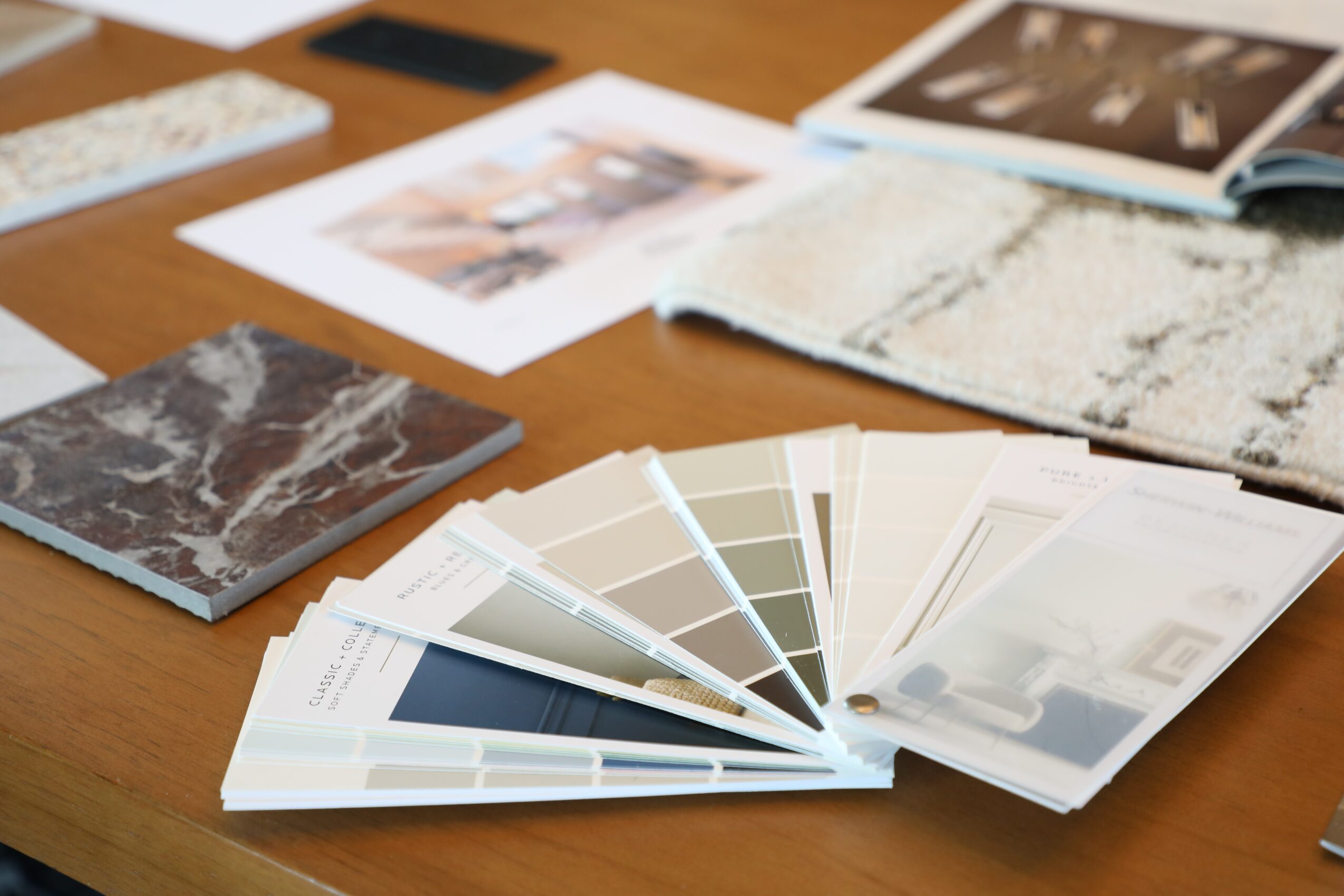Color swatch fan deck with various shades fanned out on a wooden table, surrounded by printed photographs and magazines.