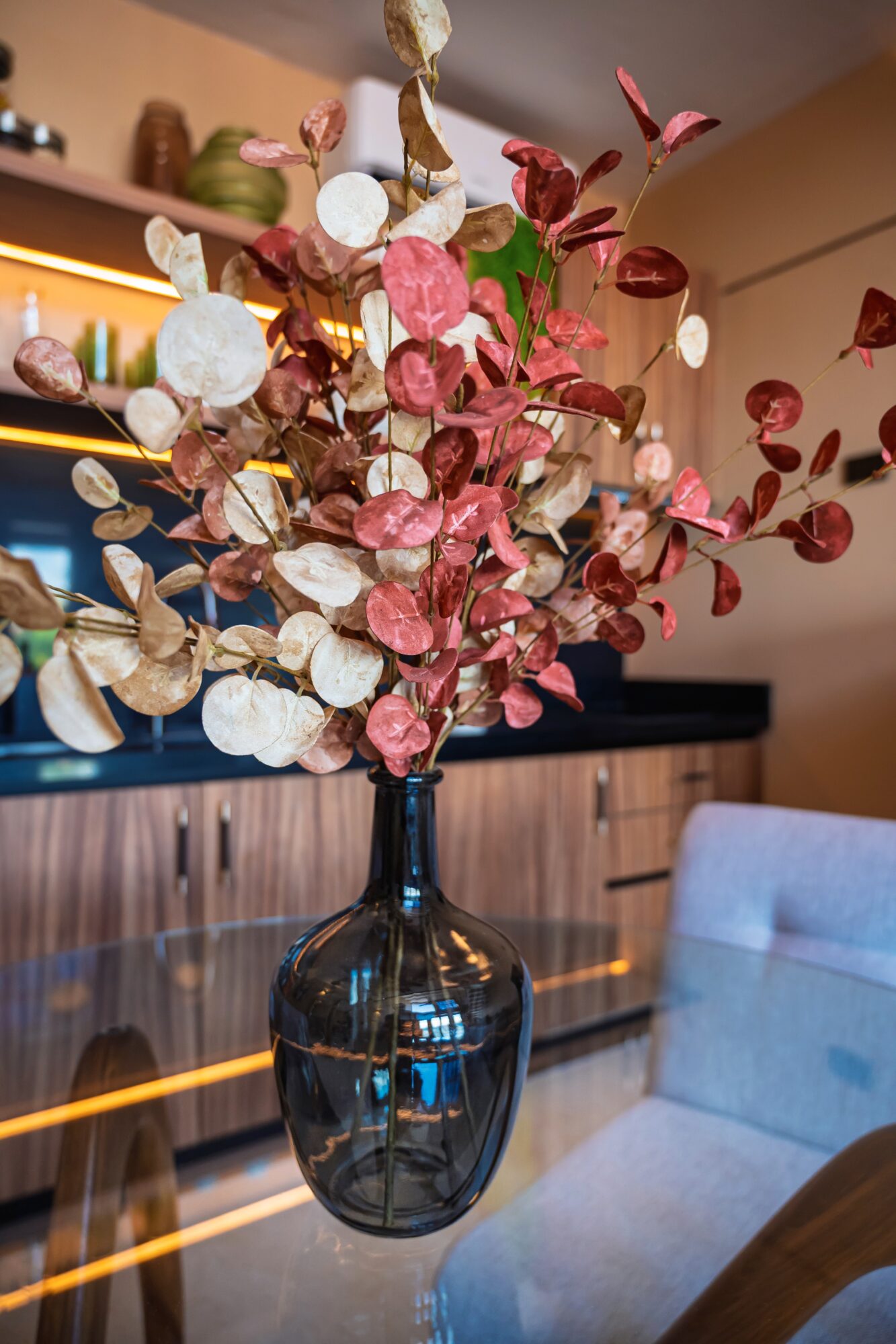 Vase with pink, white, and brown dried leaves and seed pods on a table, background of a modern interior.
