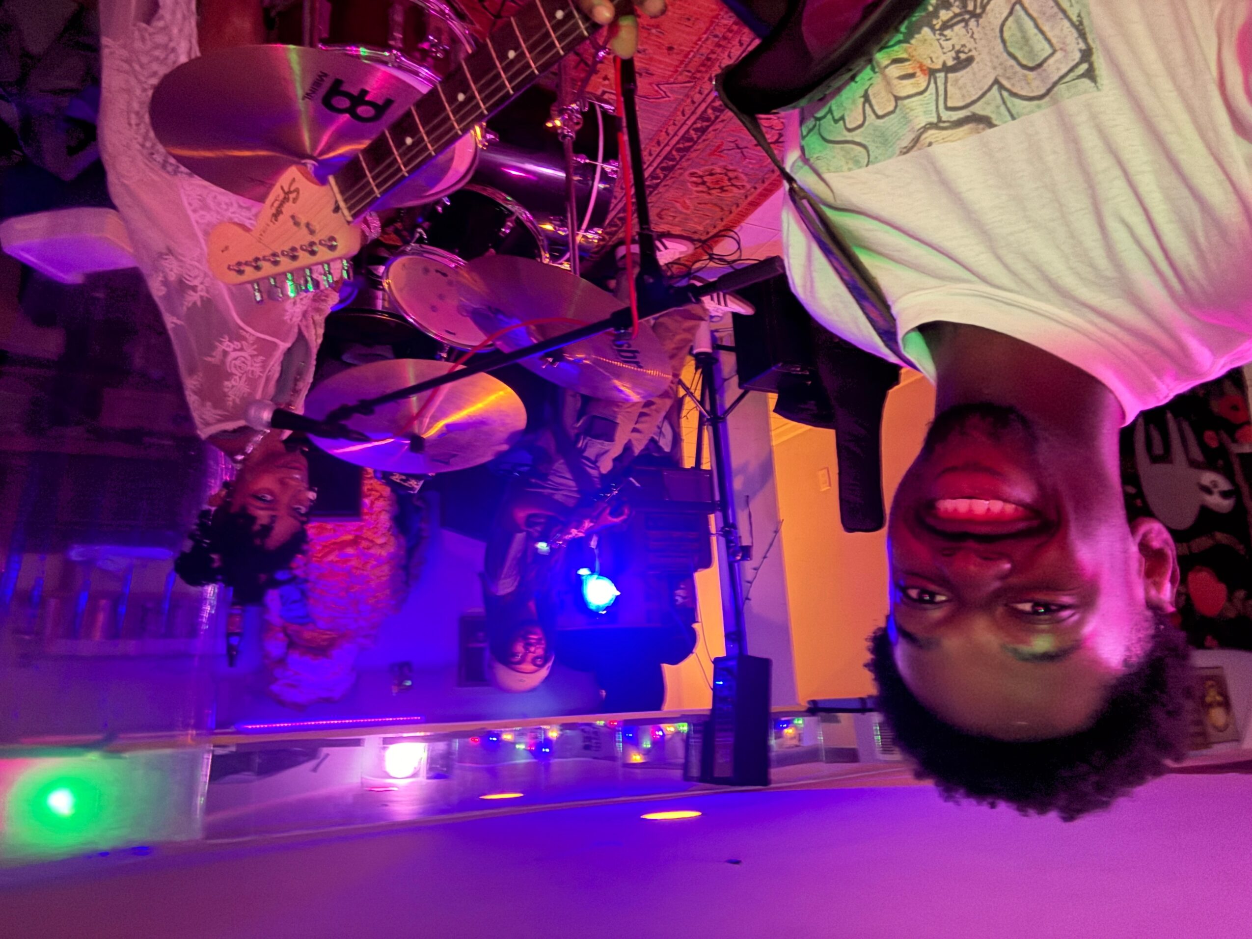 A group of people performing music on stage with colorful lighting, including a person smiling at the camera.