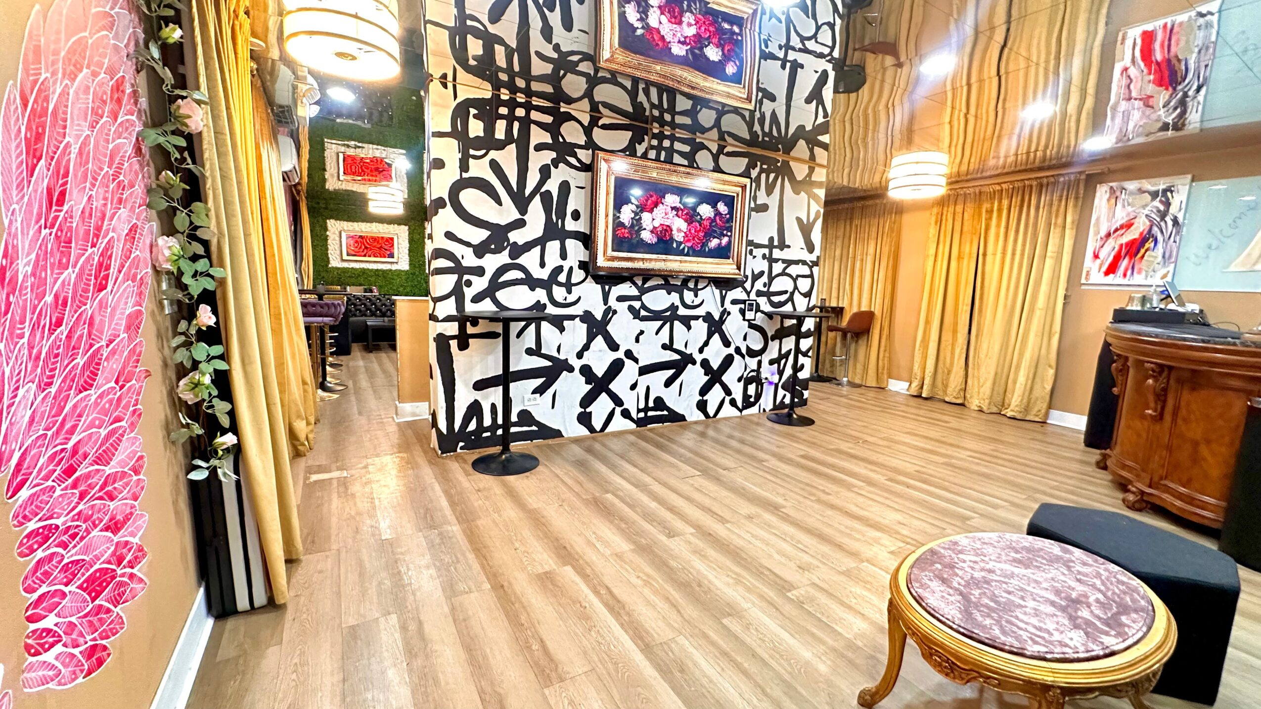 Interior of a room with wooden floors, decorated walls, two wall-mounted screens, and curtains, with a small table and chair.