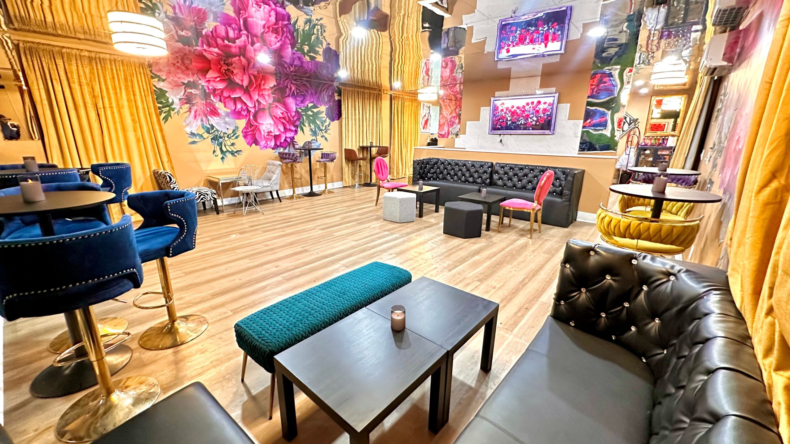 Elegant lounge with colorful floral wall, sofas, chairs, and a wooden floor, decorated with curtains and lighting fixtures.