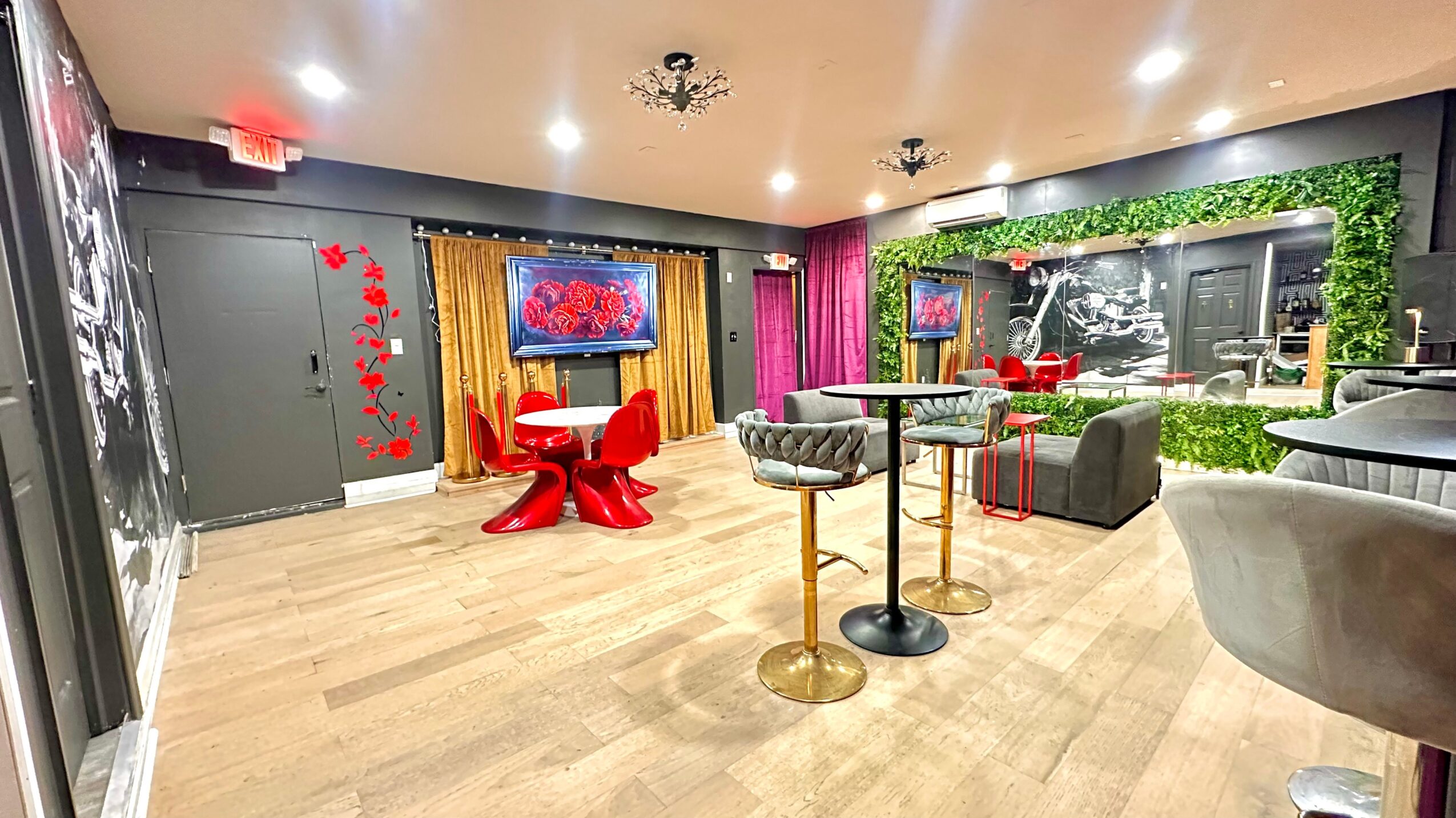 Modern lounge with colorful curtains, red tables, gray and black seating, and a green wall with a waterfall feature.