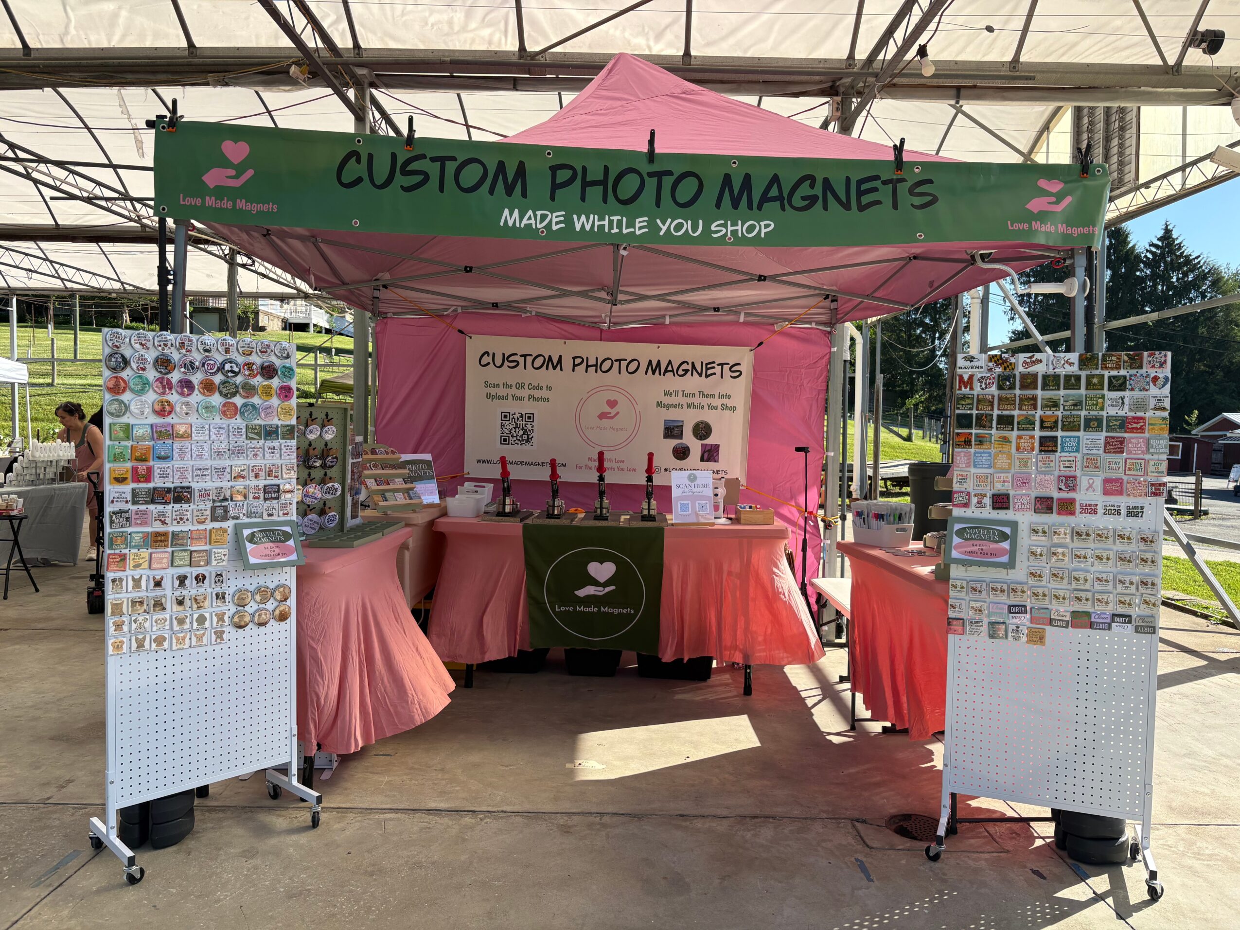 Pink tent with a sign reading 'Custom Photo Magnets' and display boards with various magnet designs.