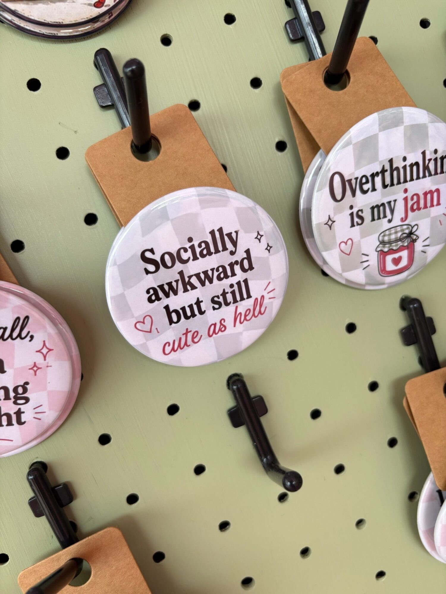 Round badge with social work message, attached to a brown paper backing, on a green pegboard with black hooks.