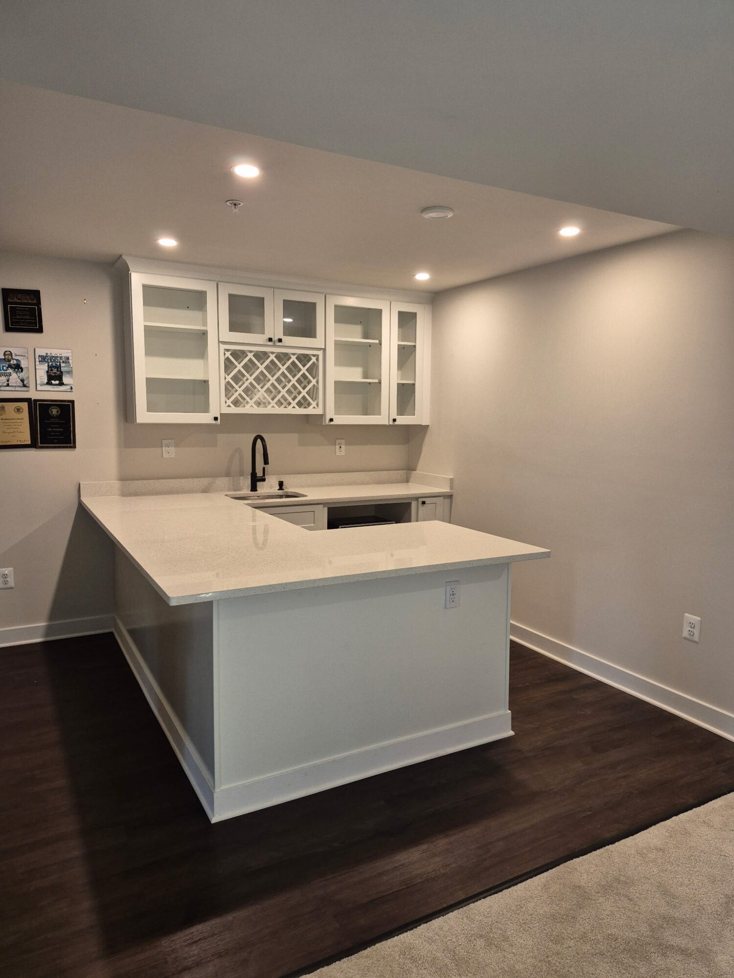Kitchen with white cabinets, island, dark wood floor, and ceiling lights, viewed from a corner.