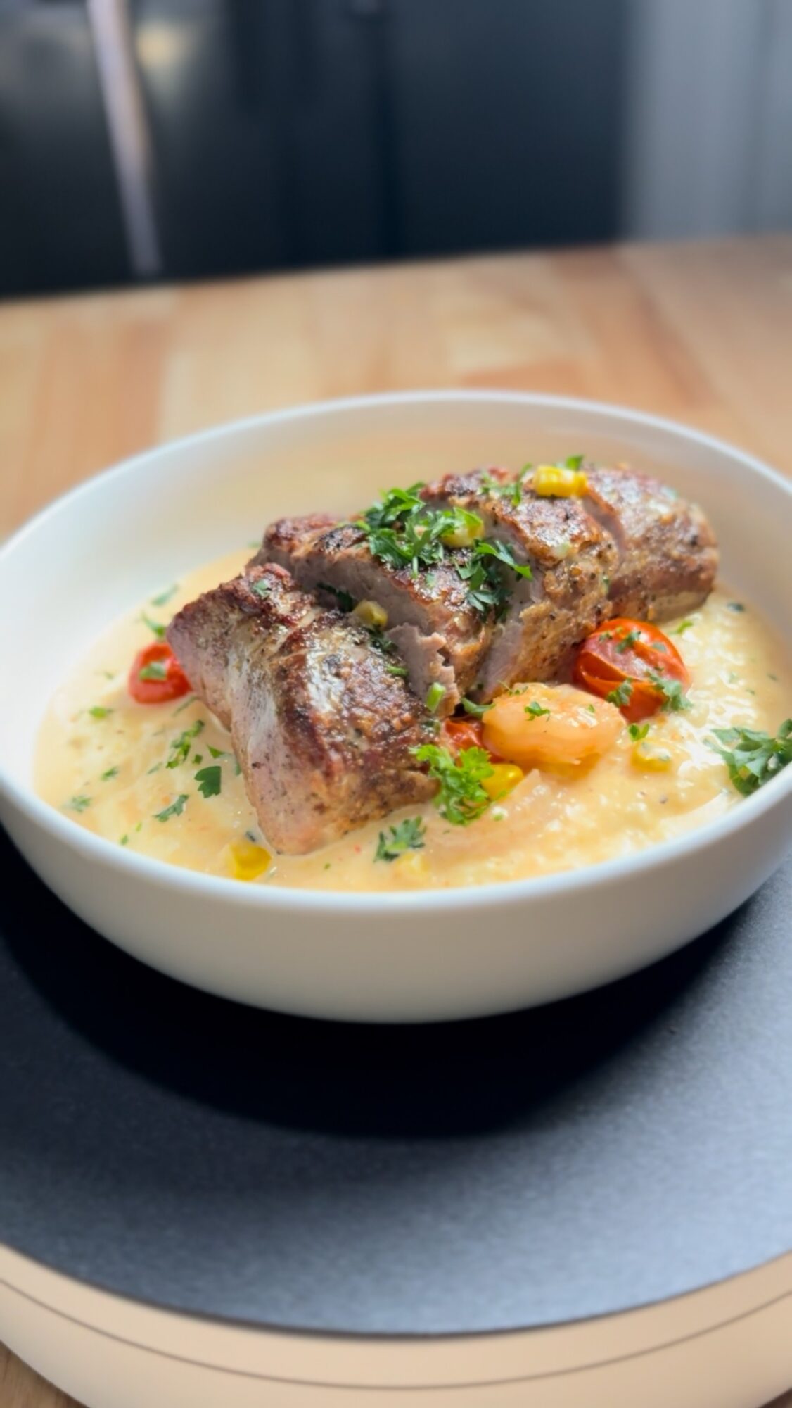 Bowl of cooked meat with vegetables and herbs in a creamy sauce on a wooden table.