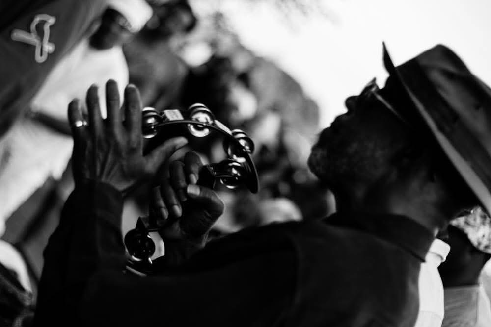 Person holding a camera, facing another person wearing a hat, in black and white.
