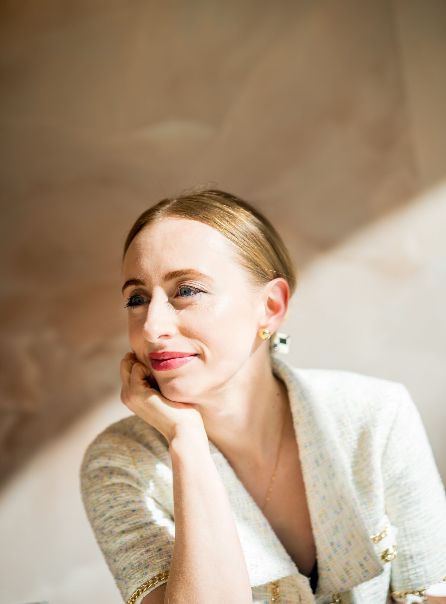 A woman with blonde hair resting her chin on her hand, smiling softly, wearing a light-colored sweater.