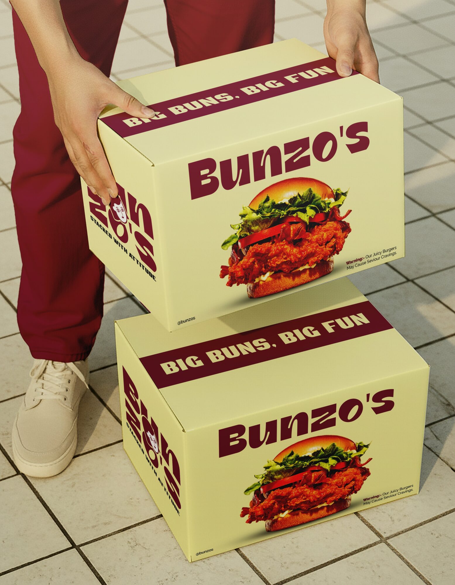 Person holding a Bunzo's box, with another box on the floor, both featuring a burger image and text, tiled floor.