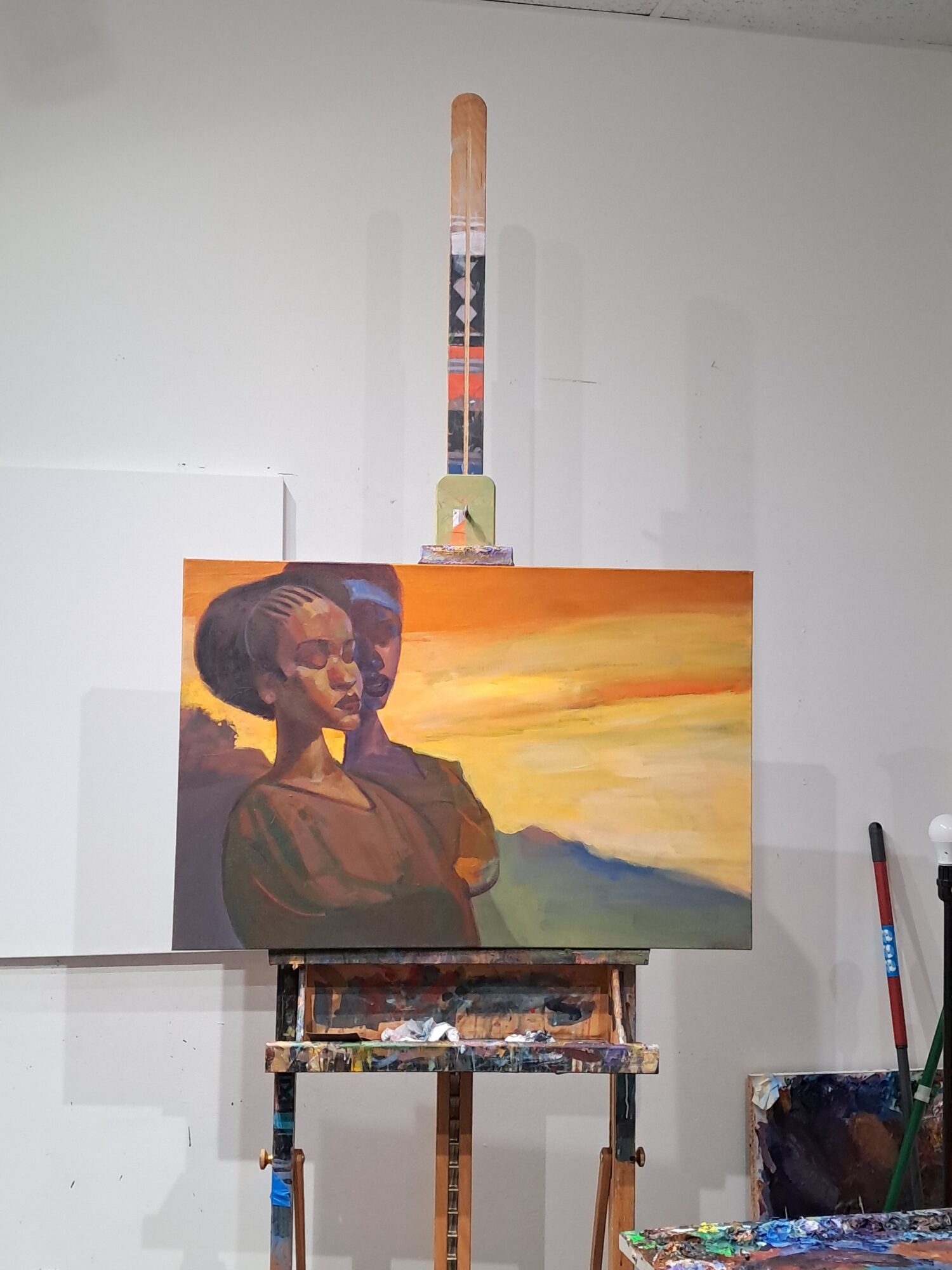 Painting of a person with a sunset background, on an easel in an art studio.