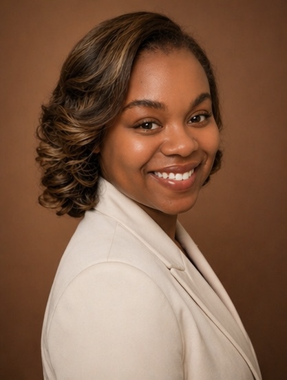 Portrait of a smiling woman with shoulder-length wavy hair, wearing a light-colored blazer, against a brown background.
