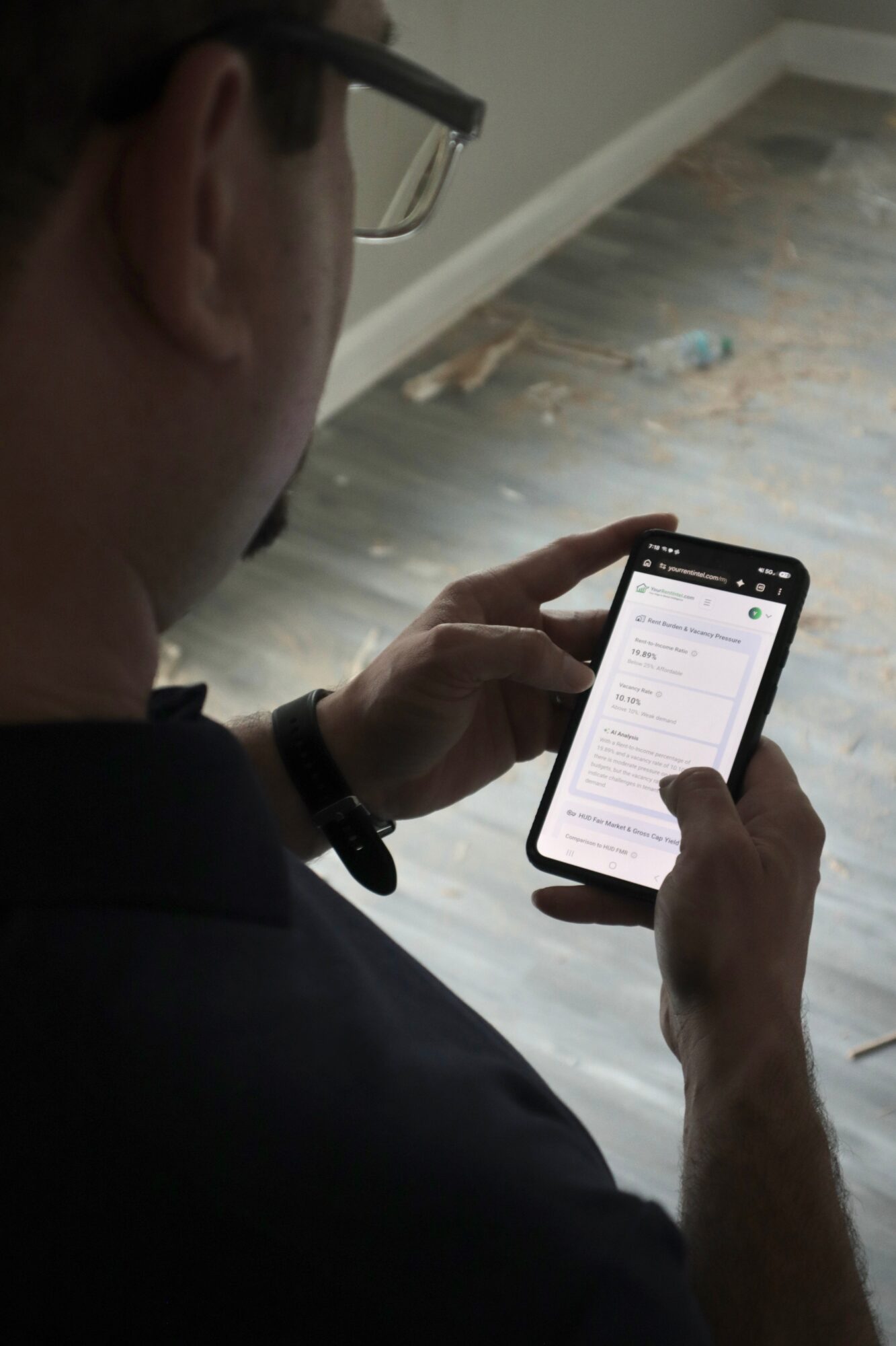 Person with glasses holding a smartphone, reading a message or email, with a wooden floor in the background.