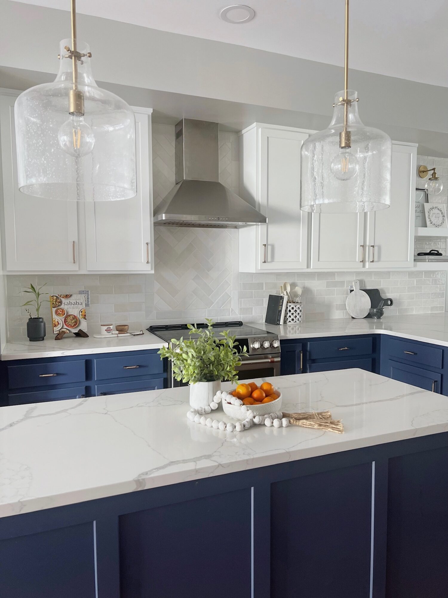 Modern kitchen with white upper cabinets, blue lower cabinets, a white countertop island, and hanging glass pendant lights.