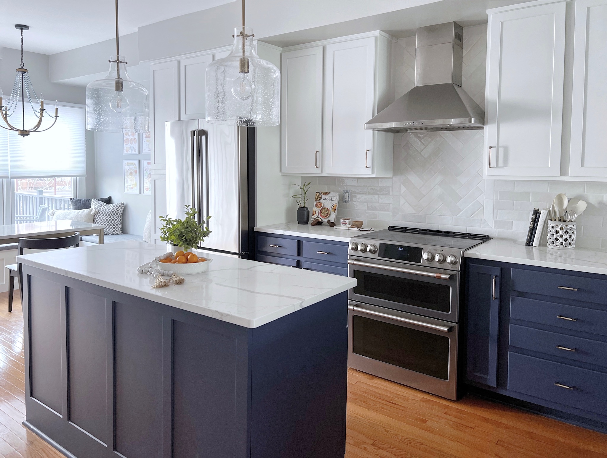 Modern kitchen with white cabinets, navy blue island, stainless steel appliances, and pendant lights, with a dining area in the background.
