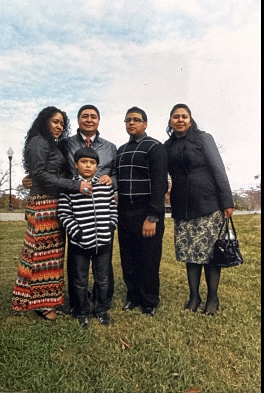 Group of five people standing outdoors on grass, with cloudy sky background.