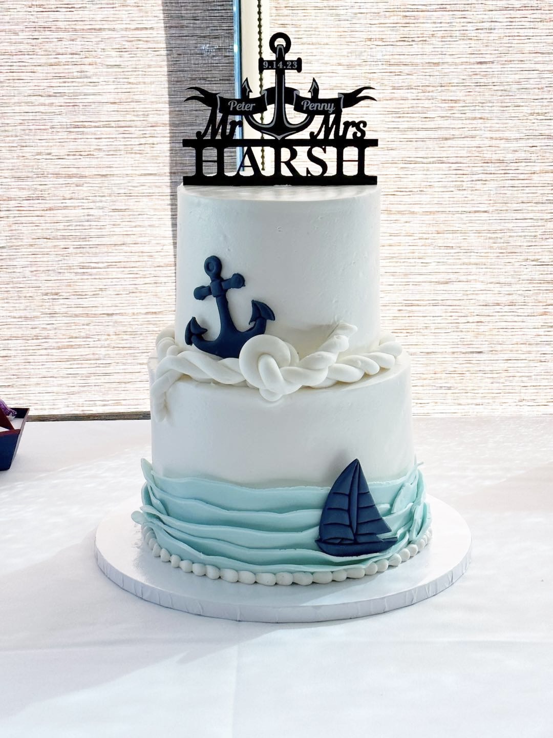 Two-tiered cake with nautical decorations, including an anchor and sailboat, topped with a black anchor and
