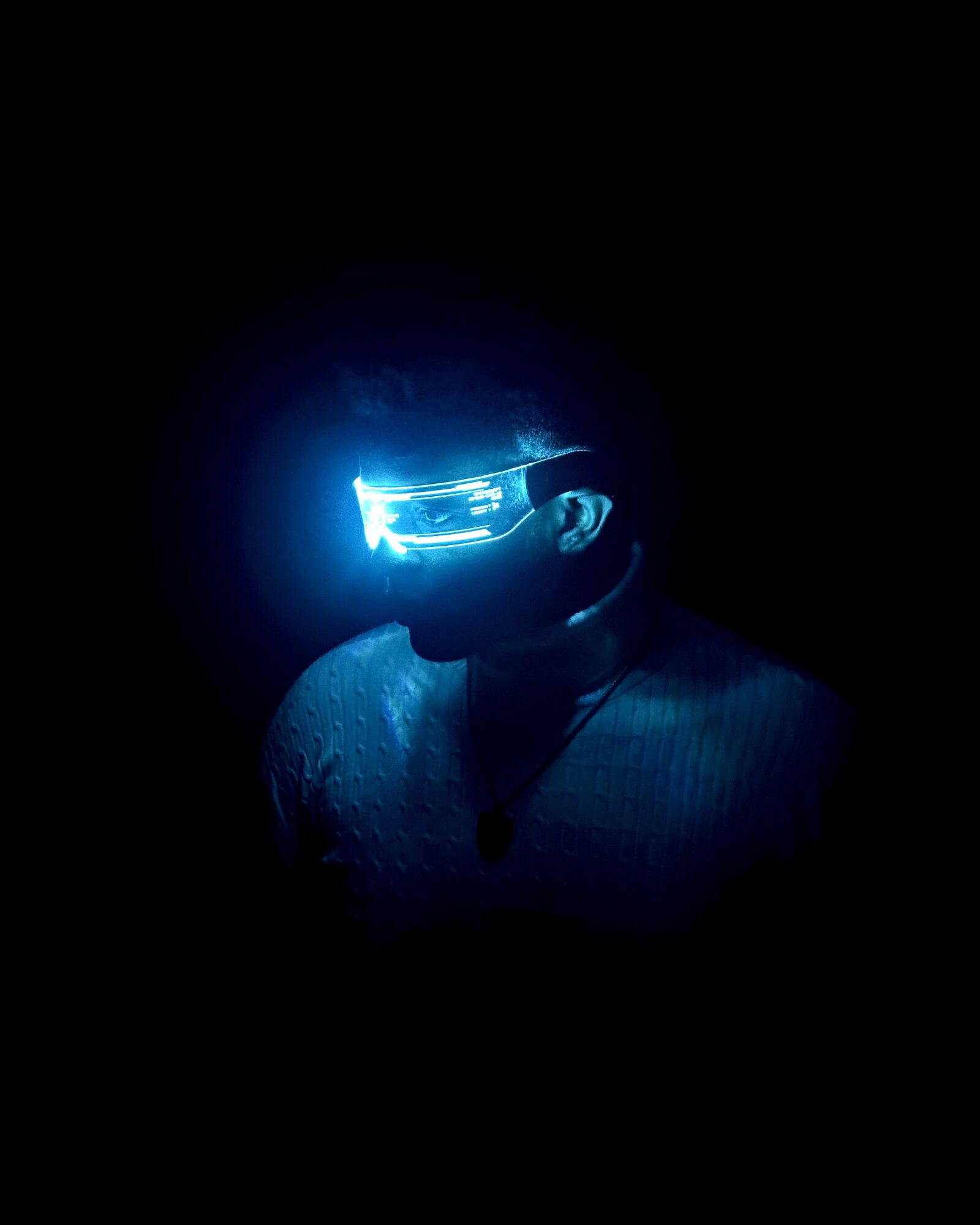 Person wearing illuminated futuristic glasses in a dark environment, with a glowing blue light reflecting on their face.