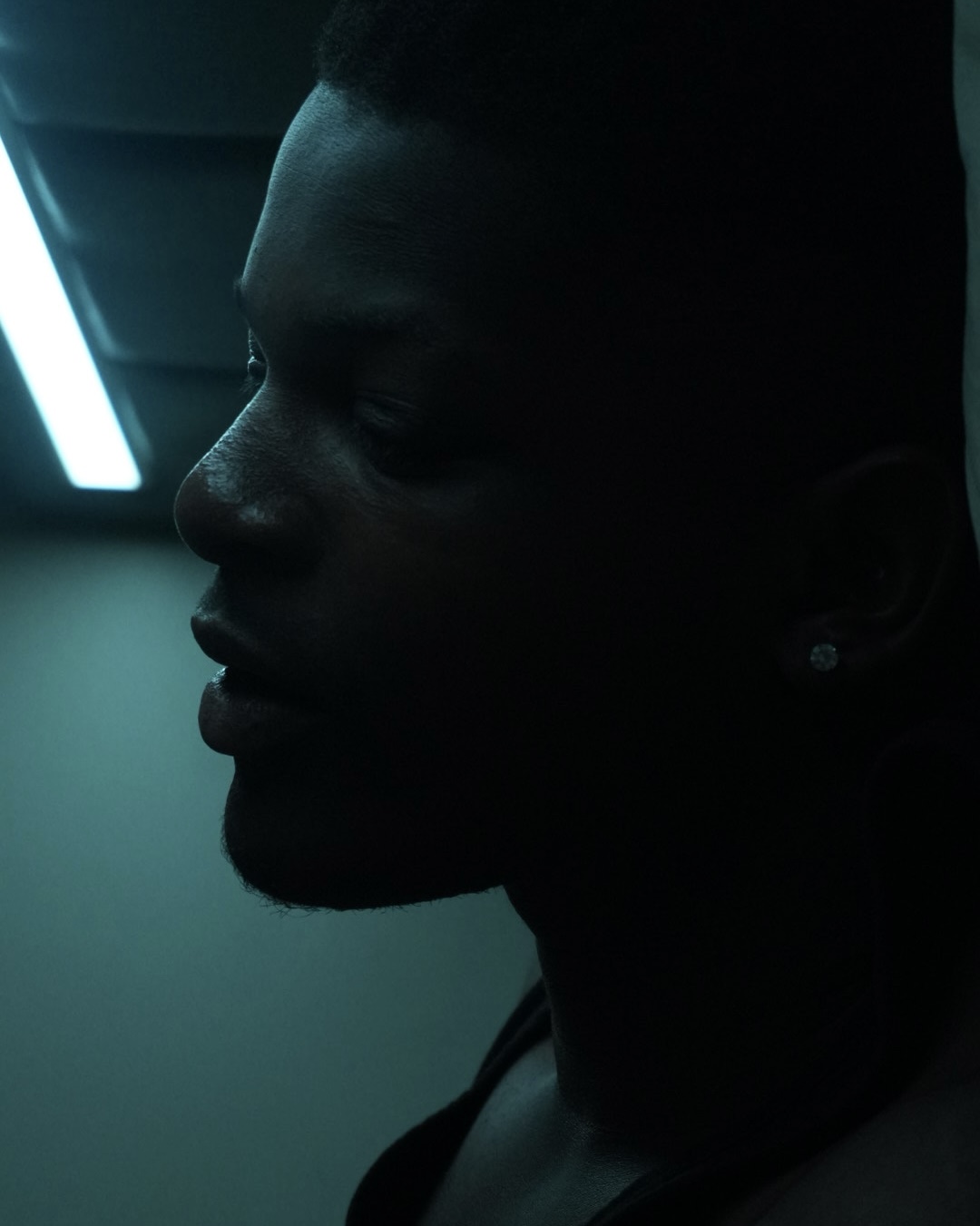 Profile of a person with short hair and earrings, dimly lit with a blue light in the background.