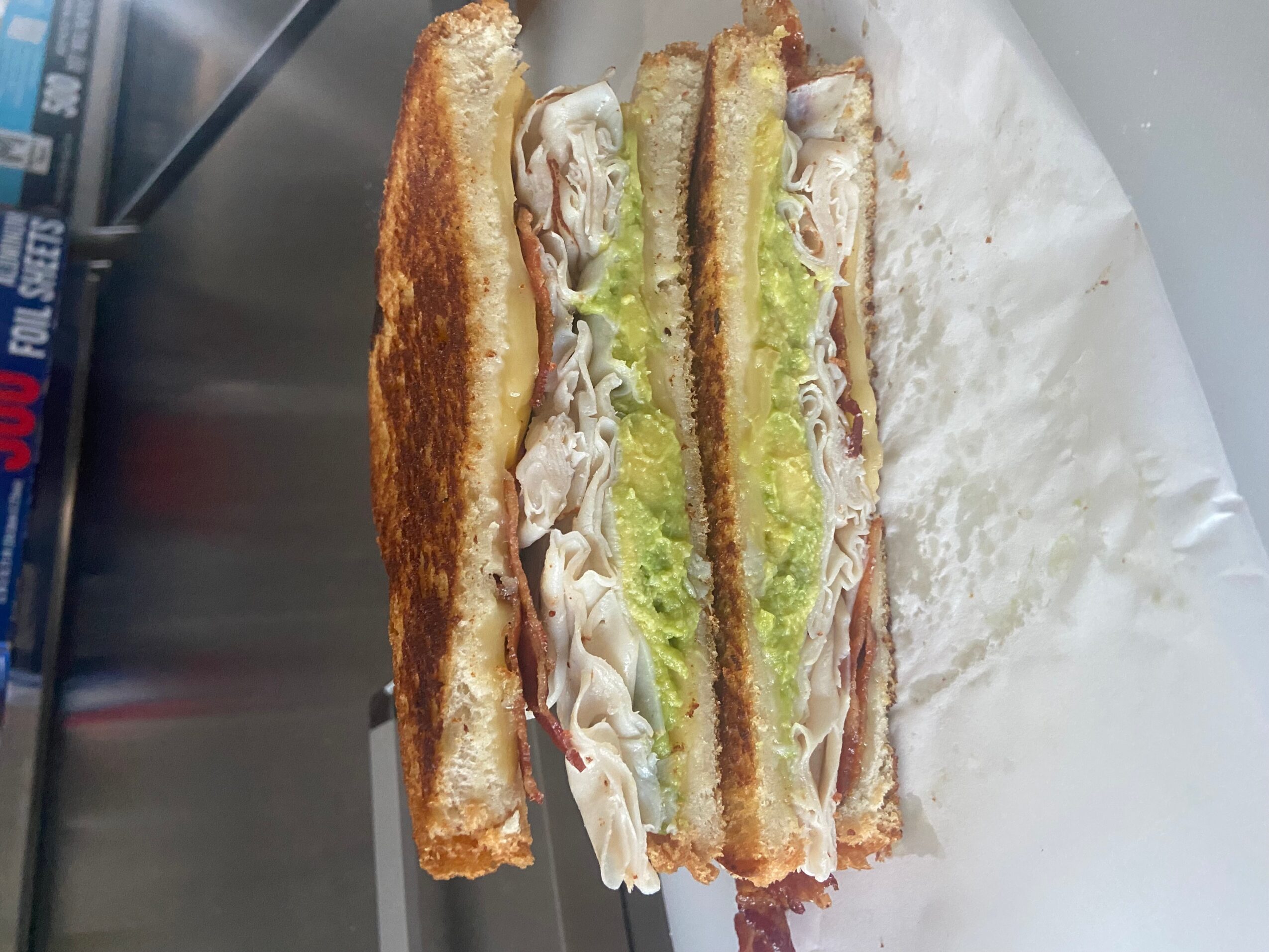 Three sandwich halves with bread, lettuce, and meat, placed on white paper, with a metallic background.