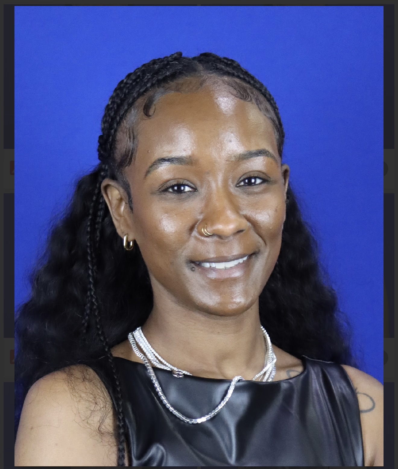 Portrait of a woman with braided hair, wearing a black top and jewelry, smiling against a blue background.