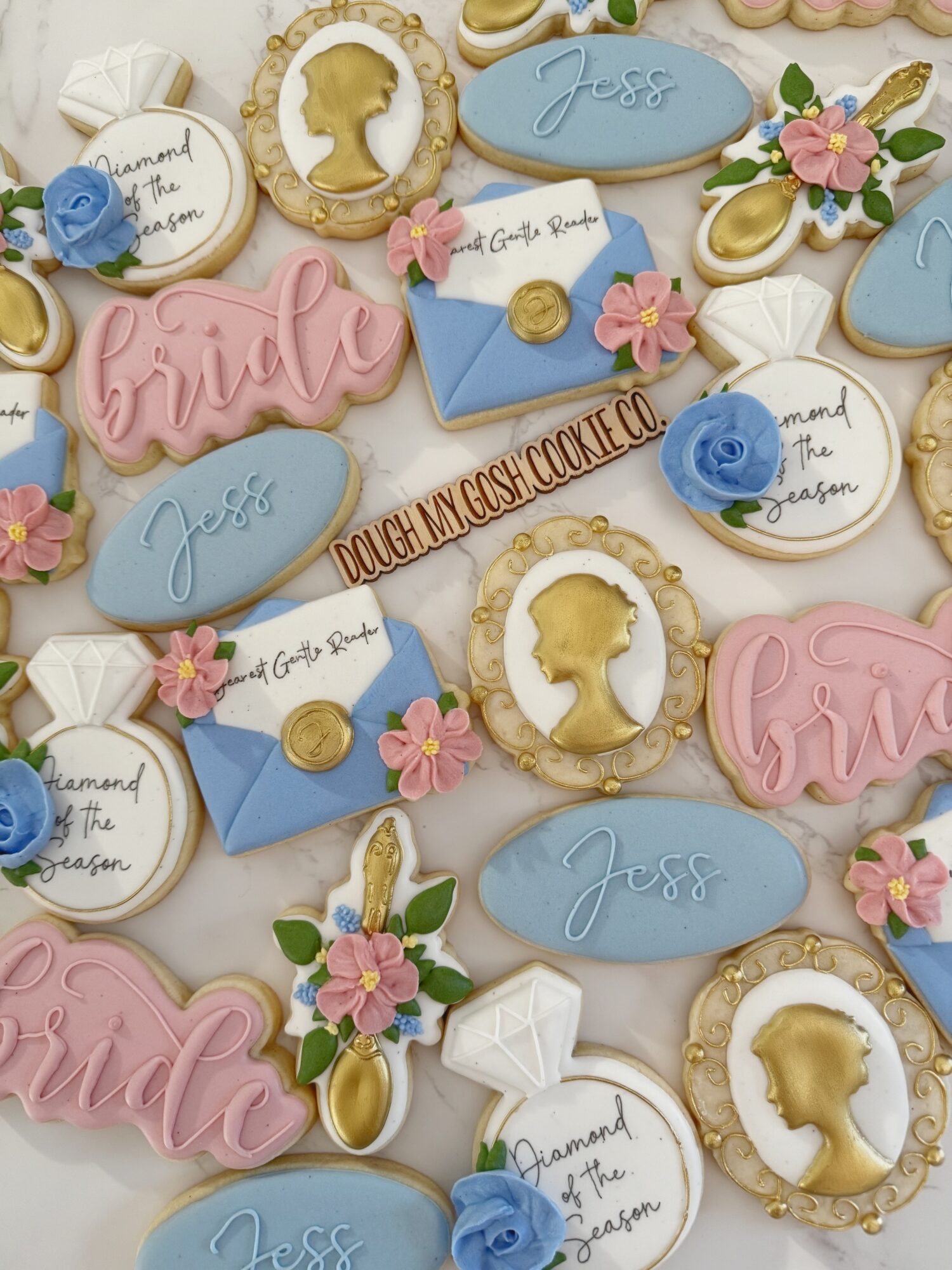 Assorted decorated cookies with bridal and baby shower themes, including flowers, silhouettes, and names, on a white background.