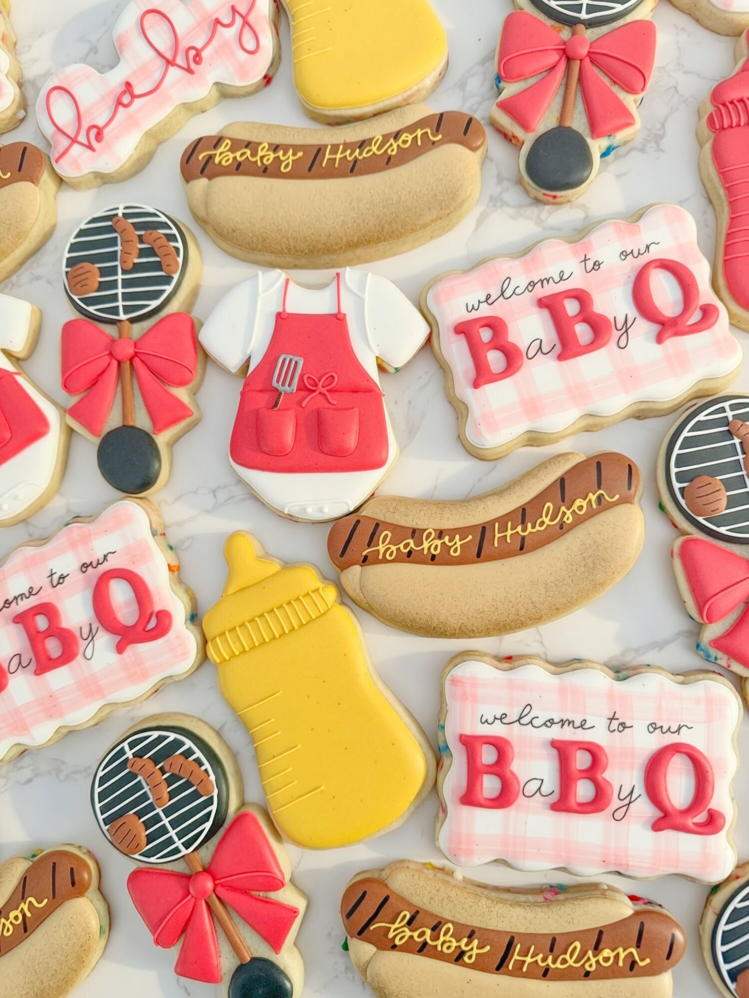 Assorted decorated cookies with baby-themed designs, including bottles, bows, and welcome signs, arranged on a surface.
