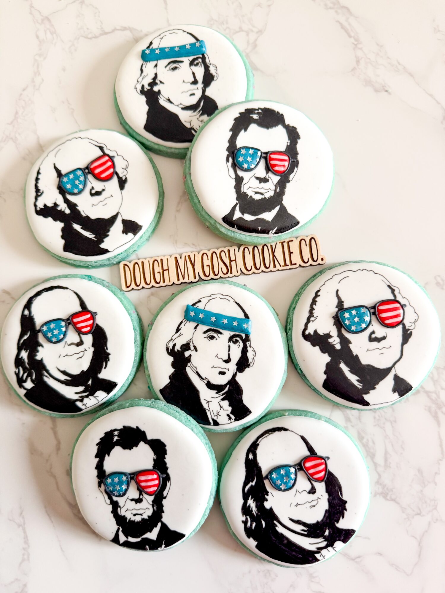 Cookies decorated with black and white portraits of a man wearing sunglasses with American flag design, on a marble surface.