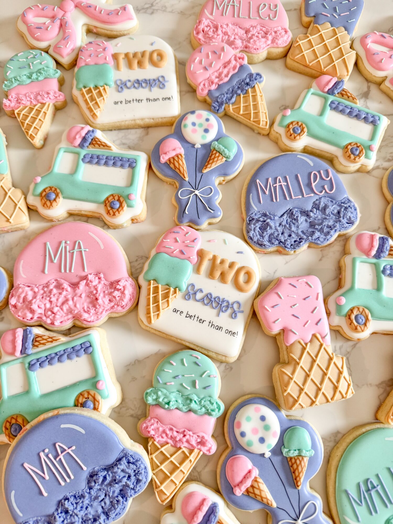 Colorful cookies shaped like ice cream cones, trucks, and balloons, with names and decorative details, arranged on a surface.