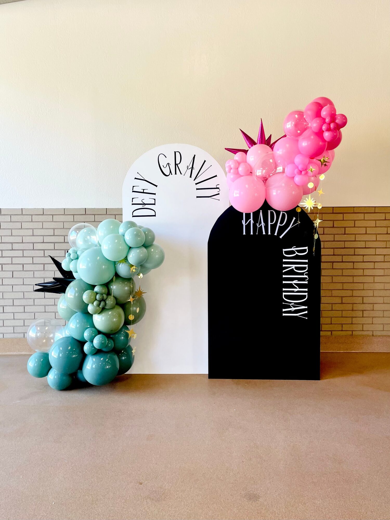 Decorative birthday display with balloon arrangements in pink and green, and a white and black backdrop with birthday messages.