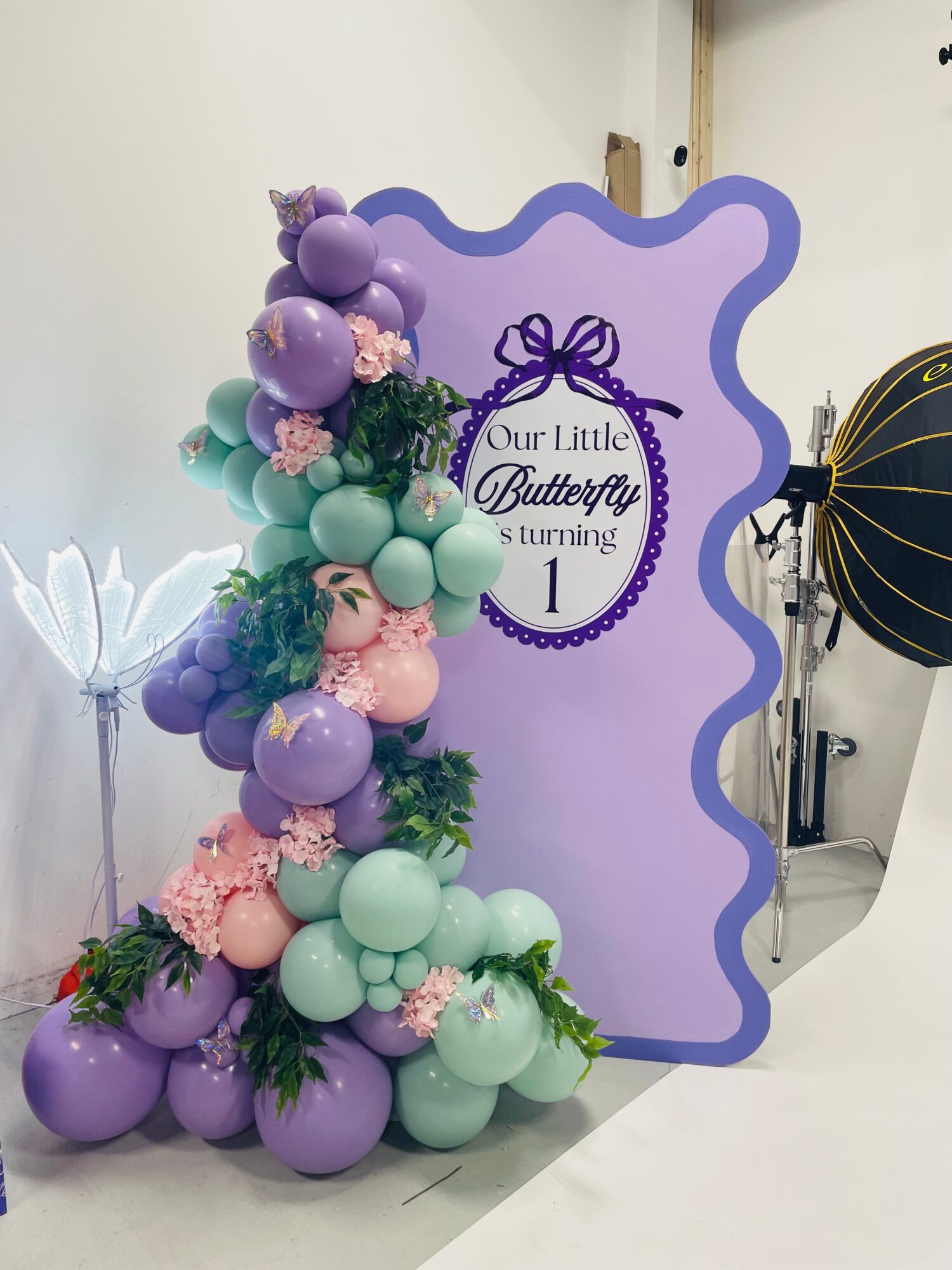 Decorative balloon arrangement with purple, pink, and green balloons next to a purple sign for a swimming event, with a butterfly theme.