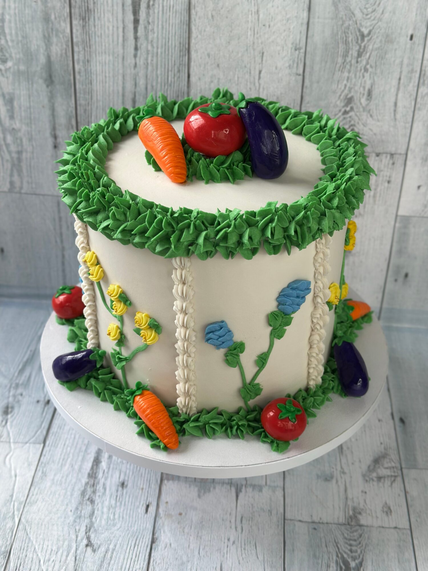 Round cake decorated with green frosting, fruit-shaped candies, and floral designs, on a white surface with a wooden background.