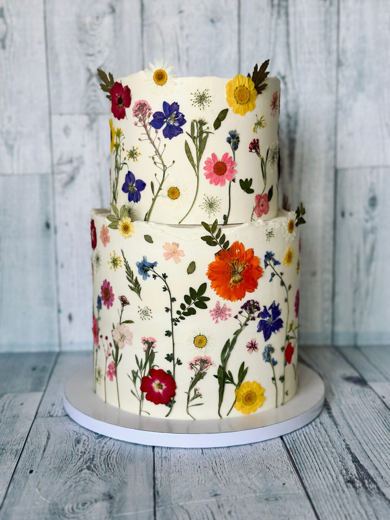 Two-tiered cake decorated with colorful floral patterns, set against a light wooden background.