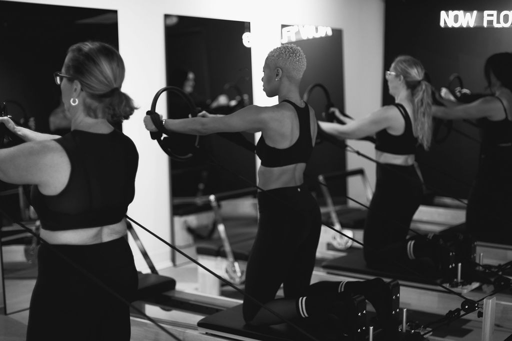 Four women in workout attire using resistance bands in a fitness studio with mirrors and equipment.