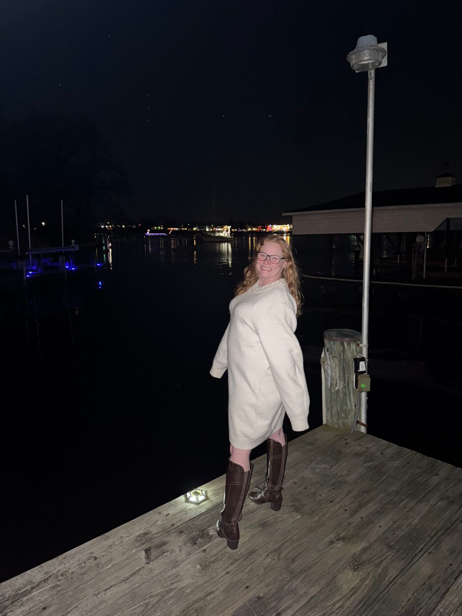 Person standing on a wooden deck at night near a lamppost with city lights in the background.