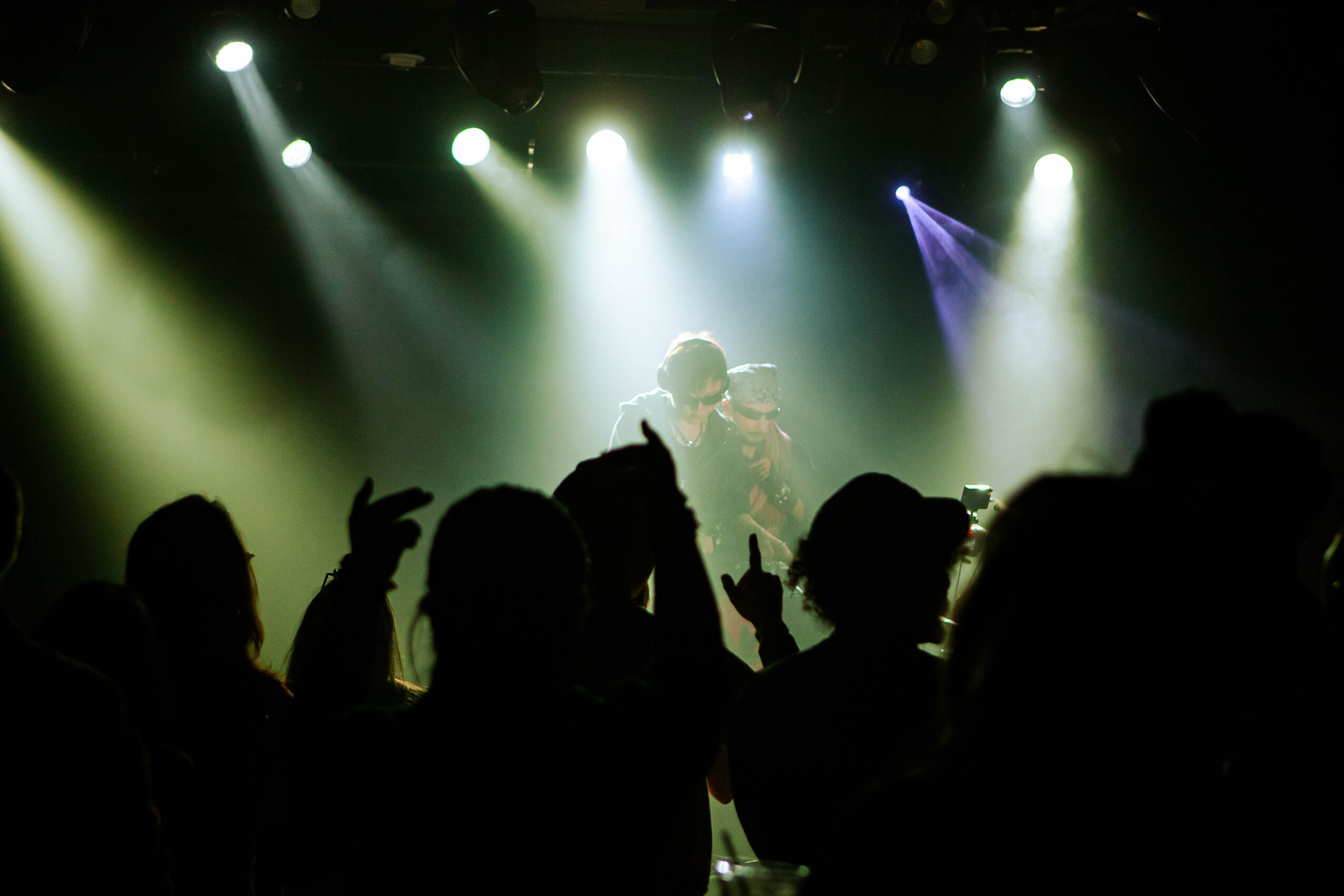 Silhouettes of people dancing and enjoying a concert with bright stage lights shining down on a performer.