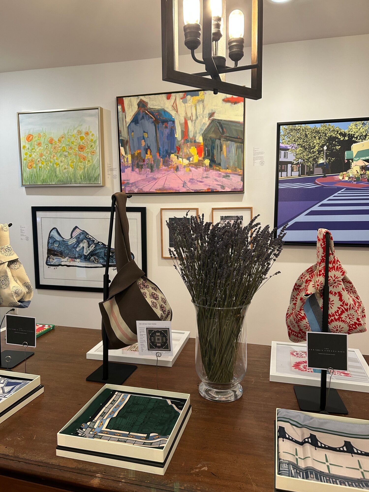 A table with a vase of dried flowers, books, and decorative items, with artwork on the wall behind.