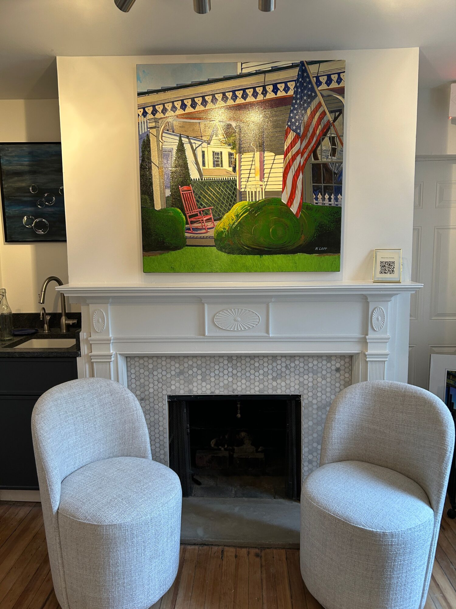 Living room with a fireplace, two white armchairs, and a television displaying an American flag and a building.