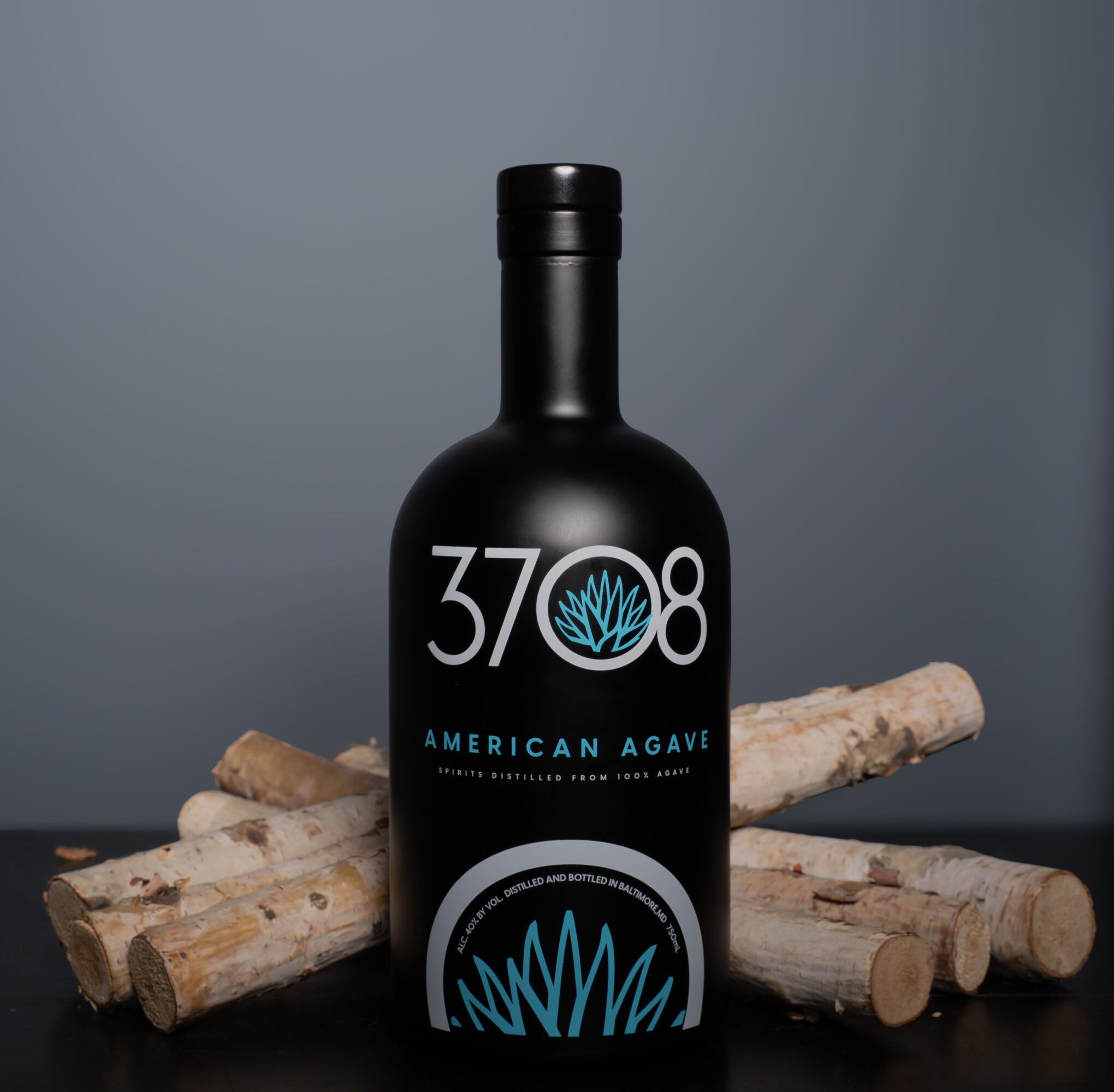 Black bottle with blue and white label, surrounded by logs, against a gray background.
