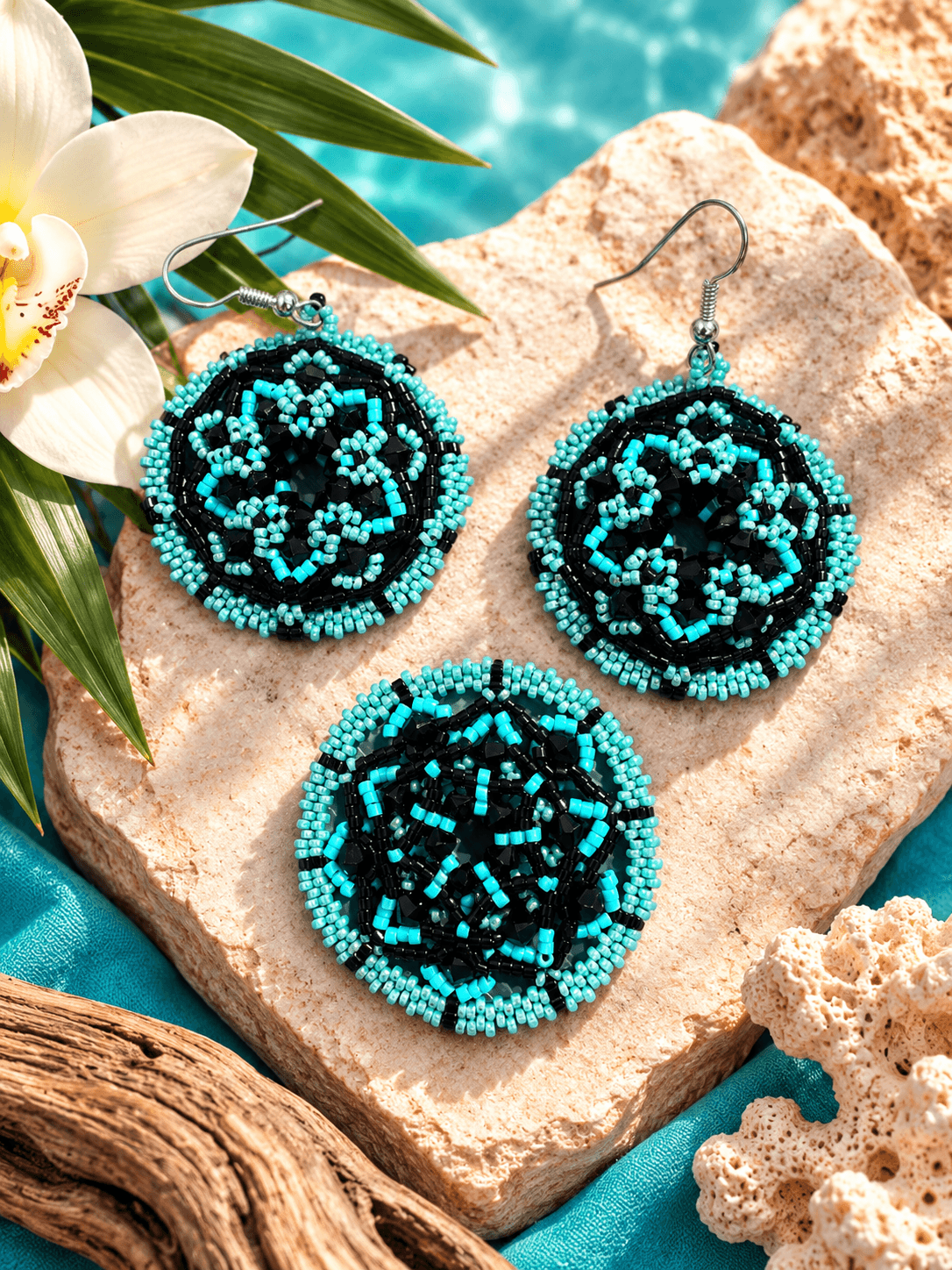 Three beaded jewelry pieces with black and turquoise beads on a stone surface, with a flower and coral nearby.