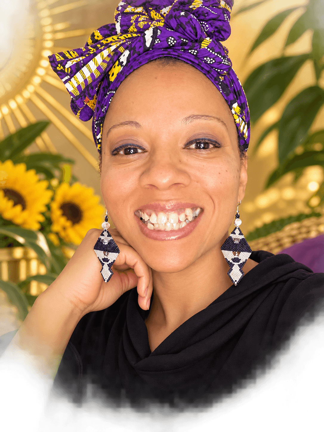 Smiling woman with a colorful headwrap, earrings, and a black top, surrounded by sunflowers and green leaves.