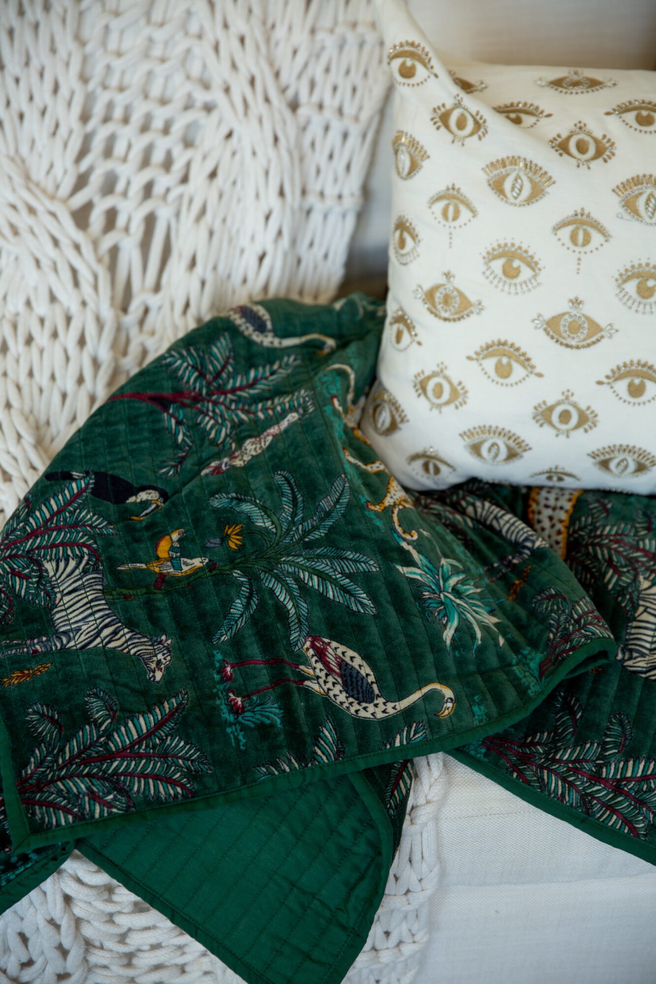 Close-up of a white woven chair with a patterned pillow and a green fabric with a jungle print.