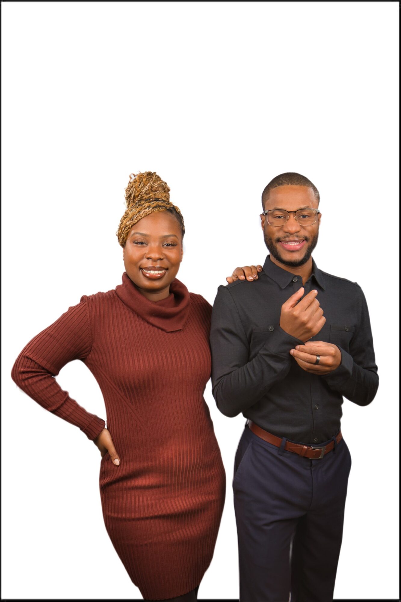 Two people standing side by side, smiling, against a white background. The woman wears a brown dress, and the man wears a black shirt and glasses.