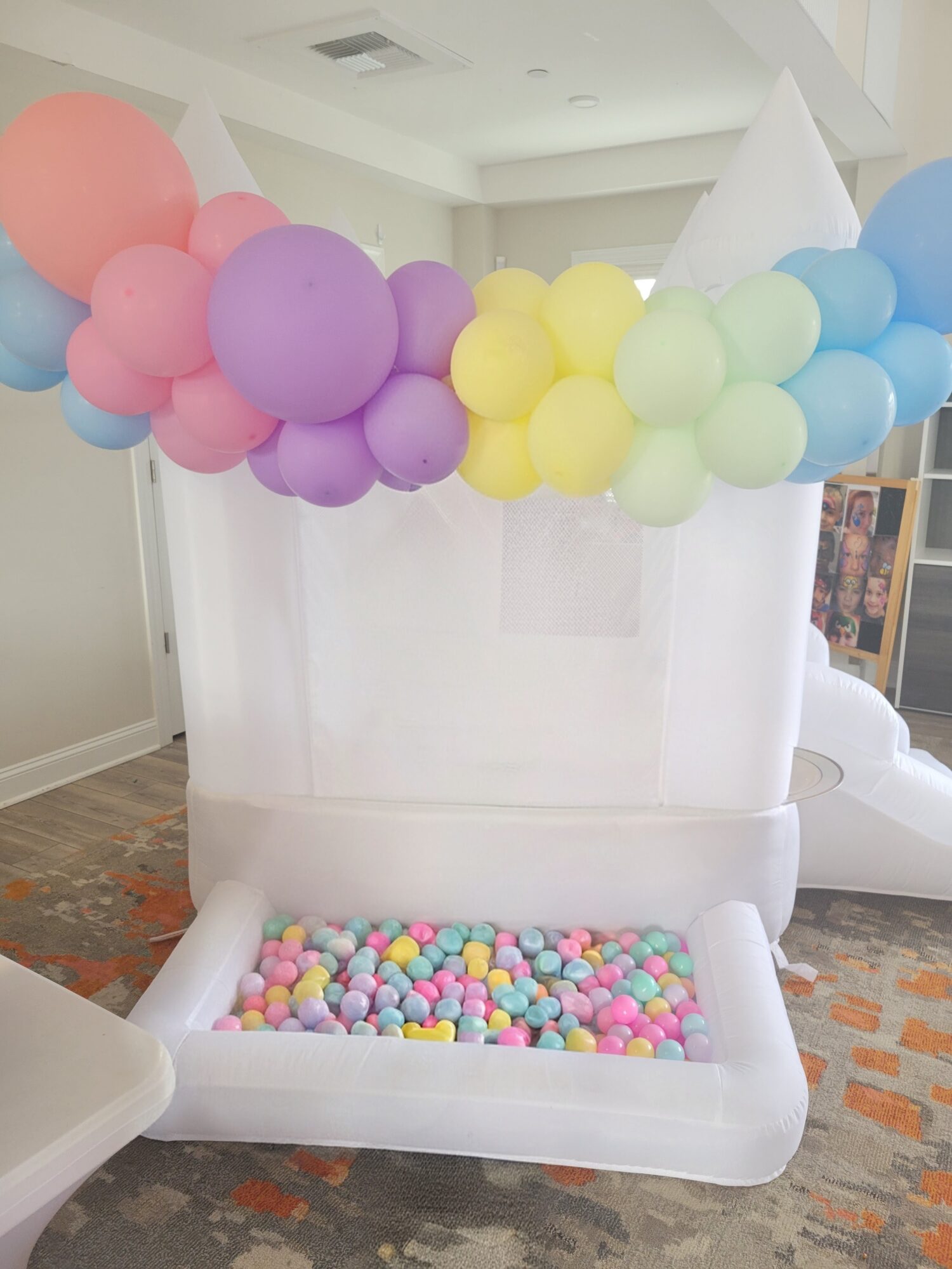 Balloon decoration with pastel-colored balloons above a white bathtub filled with small colorful balls, in a room with white walls.
